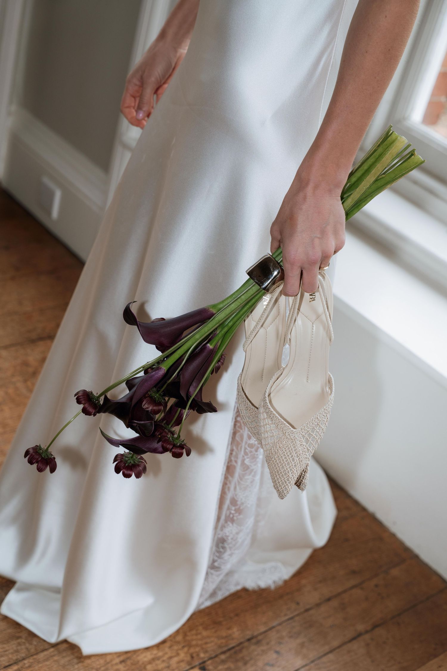 A series of close-up shots showing a white wedding dress hem and dark purple calla lilies against a wooden floor.