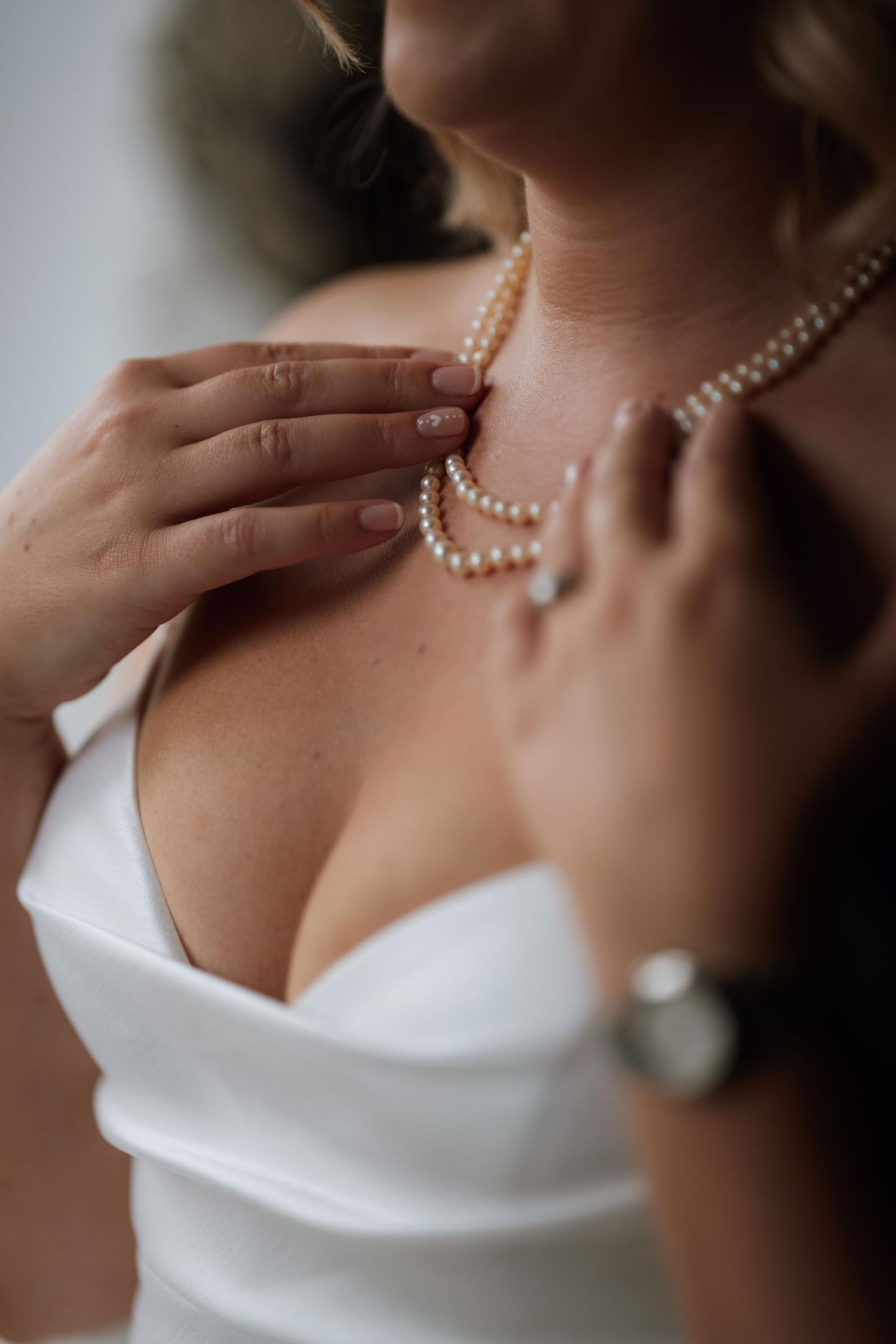 A pearl necklace adorns a neck above an elegant white sweetheart neckline in a romantic close-up shot.