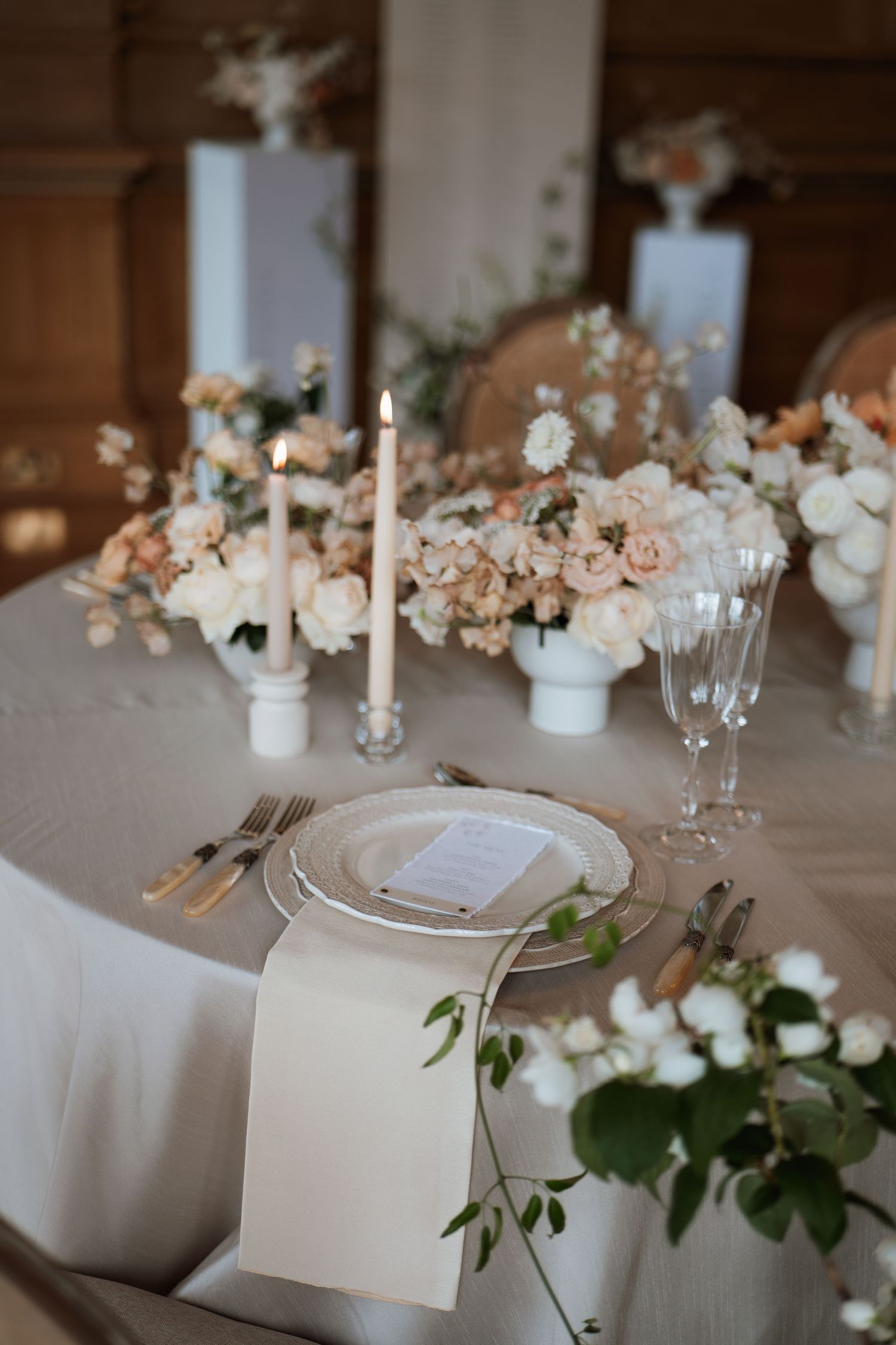 Elegant wedding table setting with white and blush floral centerpieces, taper candles, and fine china on neutral linens.