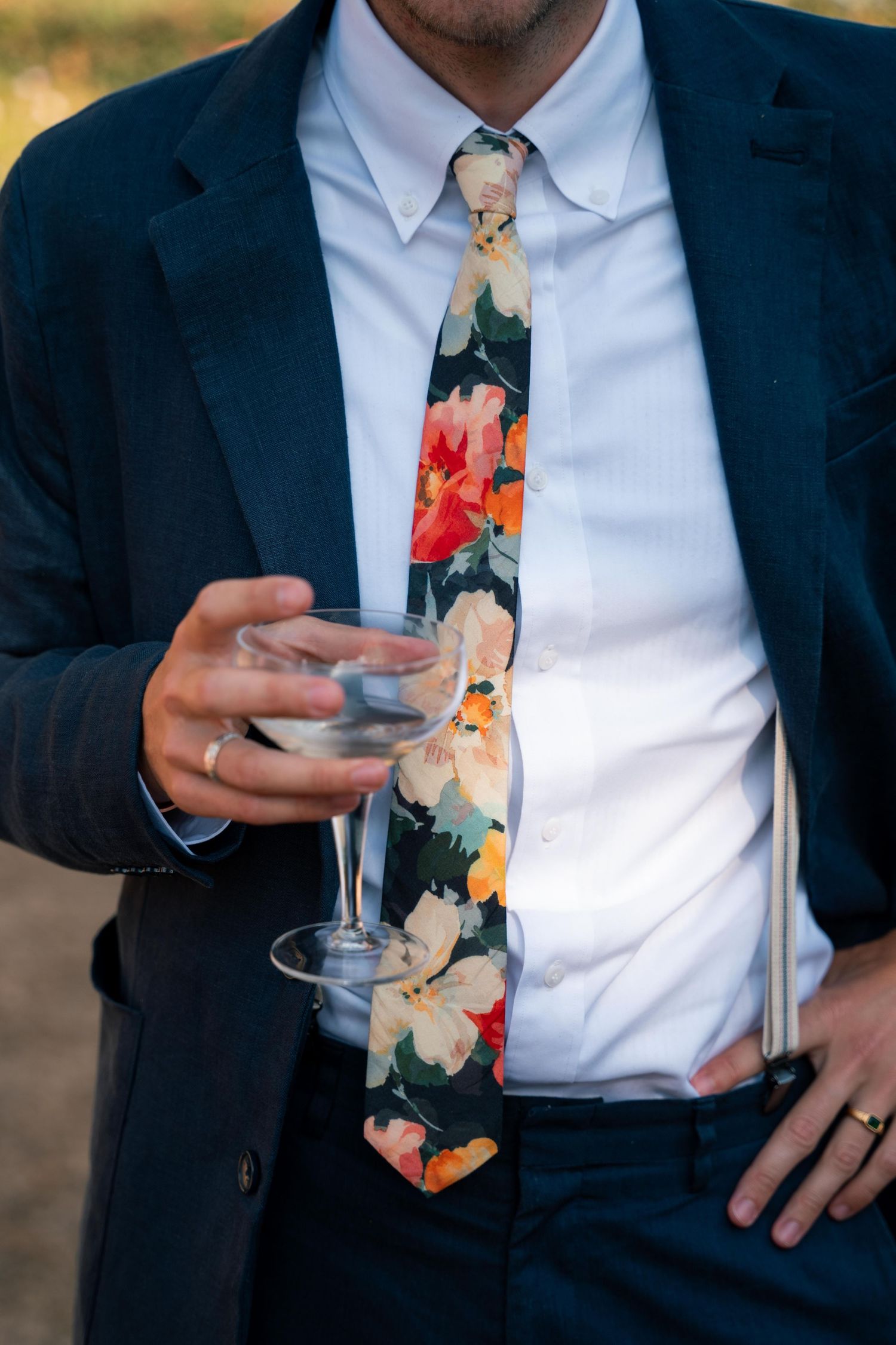 Close-up shots of person in navy suit and floral tie holding champagne glass at formal event.