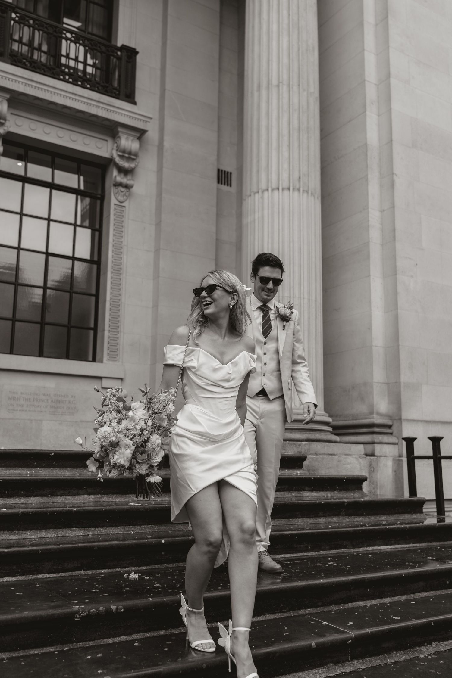 A black and white photo showing a person in white clothing running up stone steps with classical columns in the background.