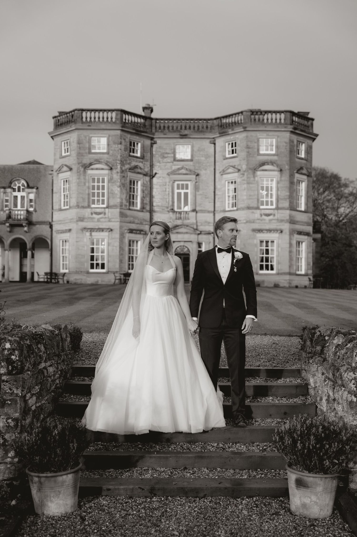Wedding couple poses in front of a grand historic mansion with elegant stone architecture.