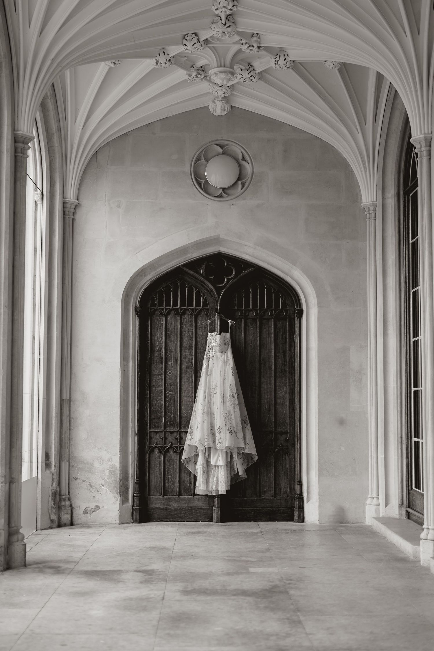 A series of white wedding dresses float ethereally in a grand Gothic corridor with vaulted ceilings and arched doorways.