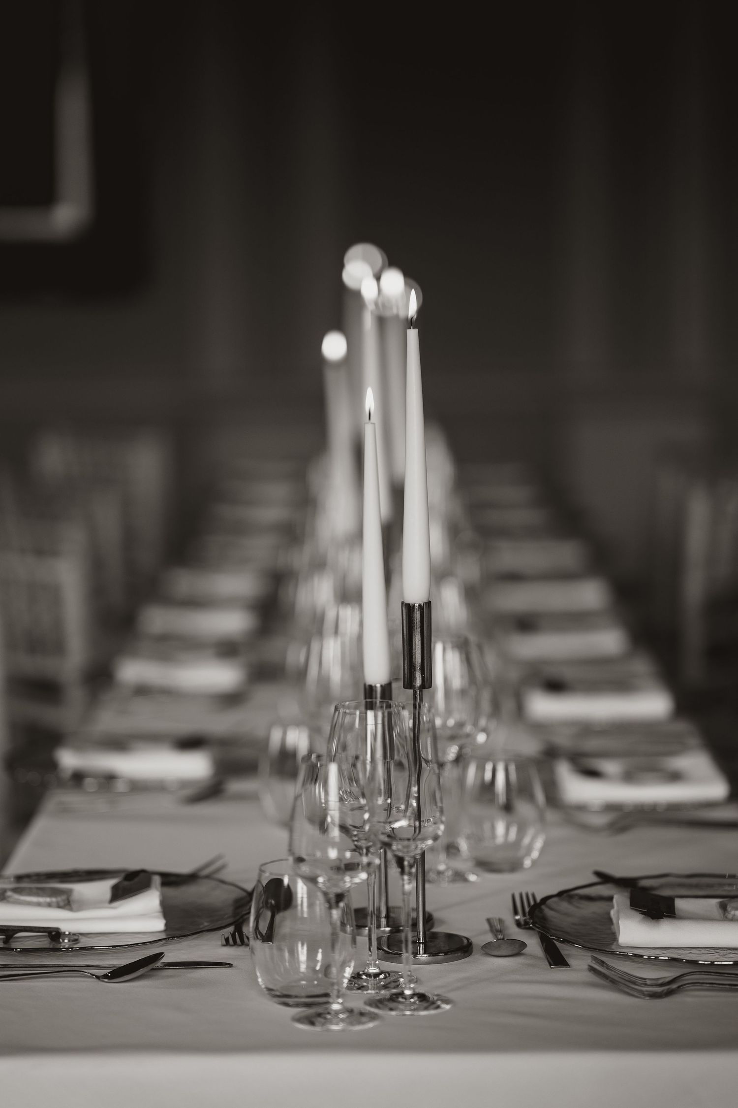 Elegant black and white table settings with tall white candles and wine glasses arranged for a formal dining event.