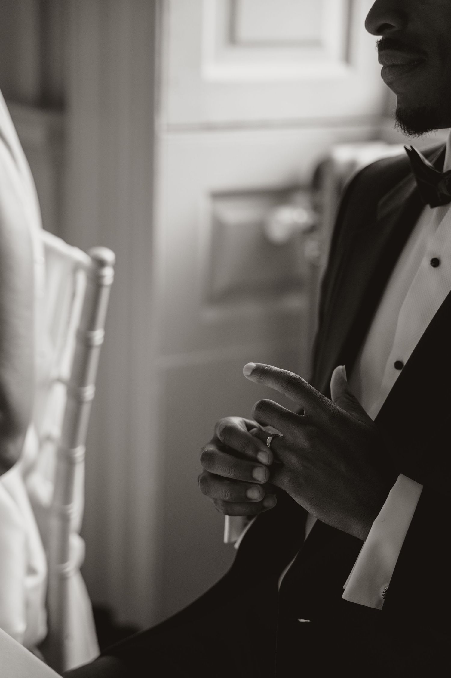 Close-up black and white shot of hands adjusting cufflinks on a formal tuxedo sleeve.