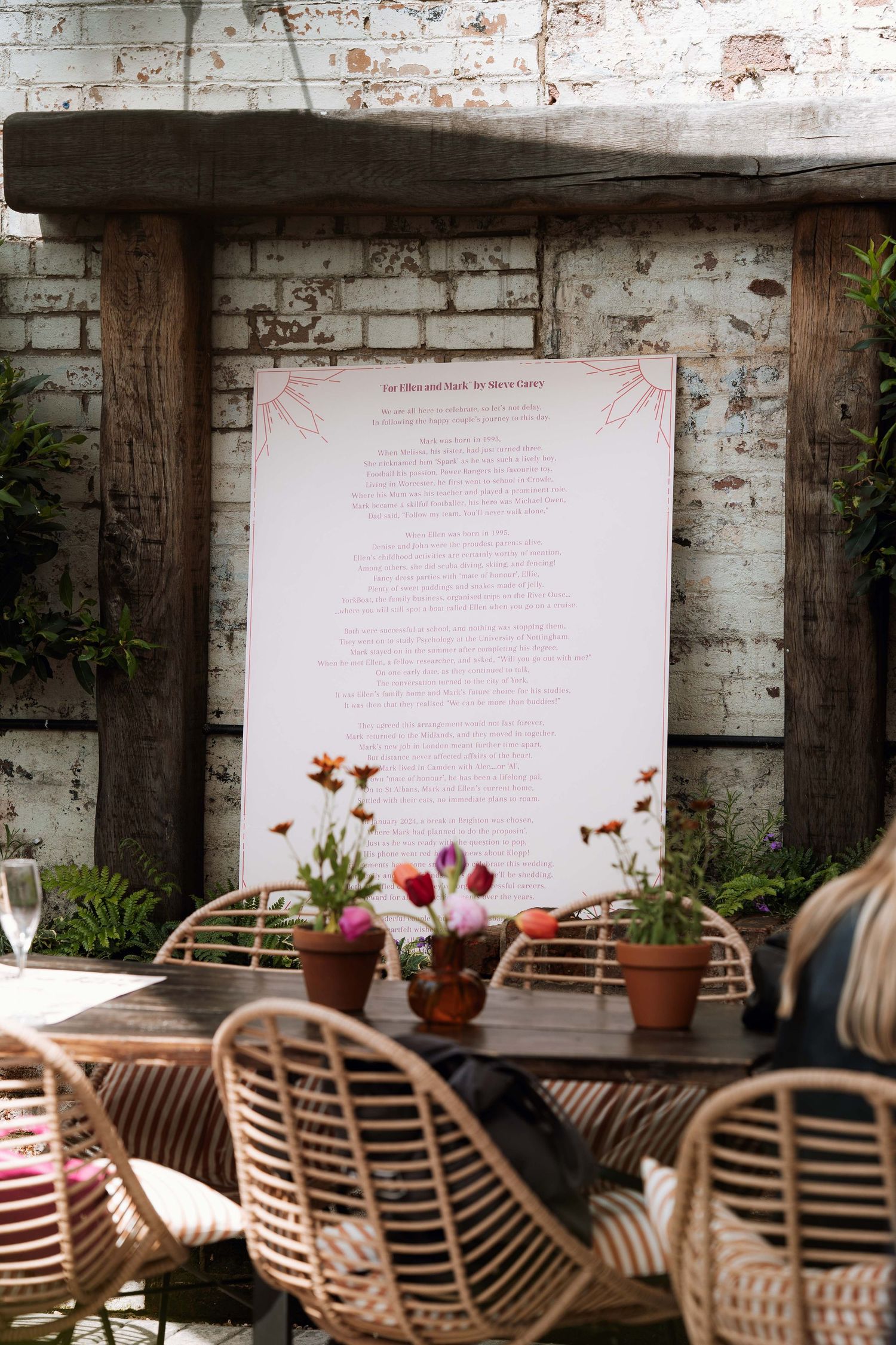 Rustic outdoor seating area with rattan chairs and potted plants against a weathered brick wall with text panels.