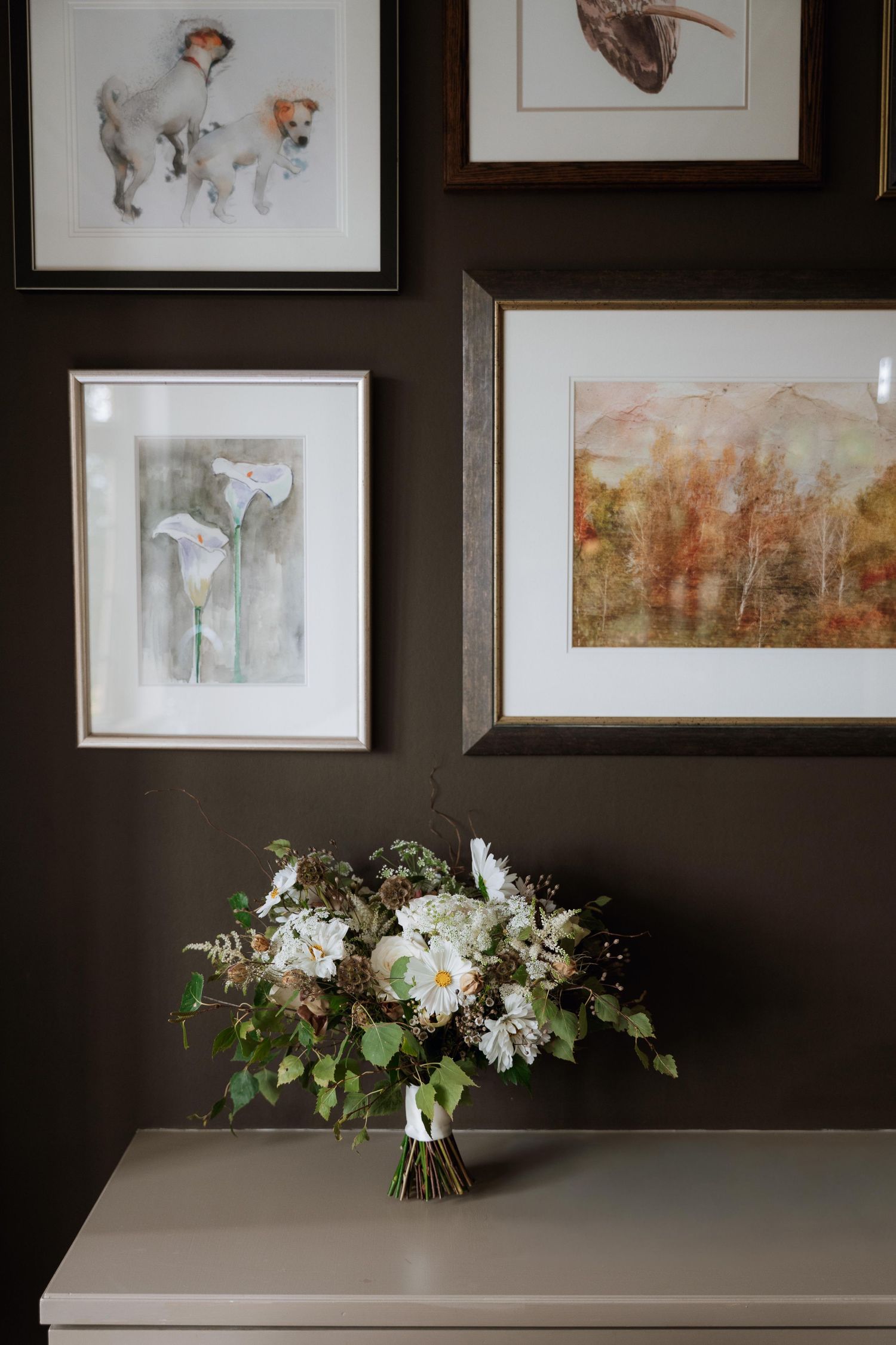 Gallery wall of framed artwork and sketches hangs above a white table decorated with fresh floral arrangements.