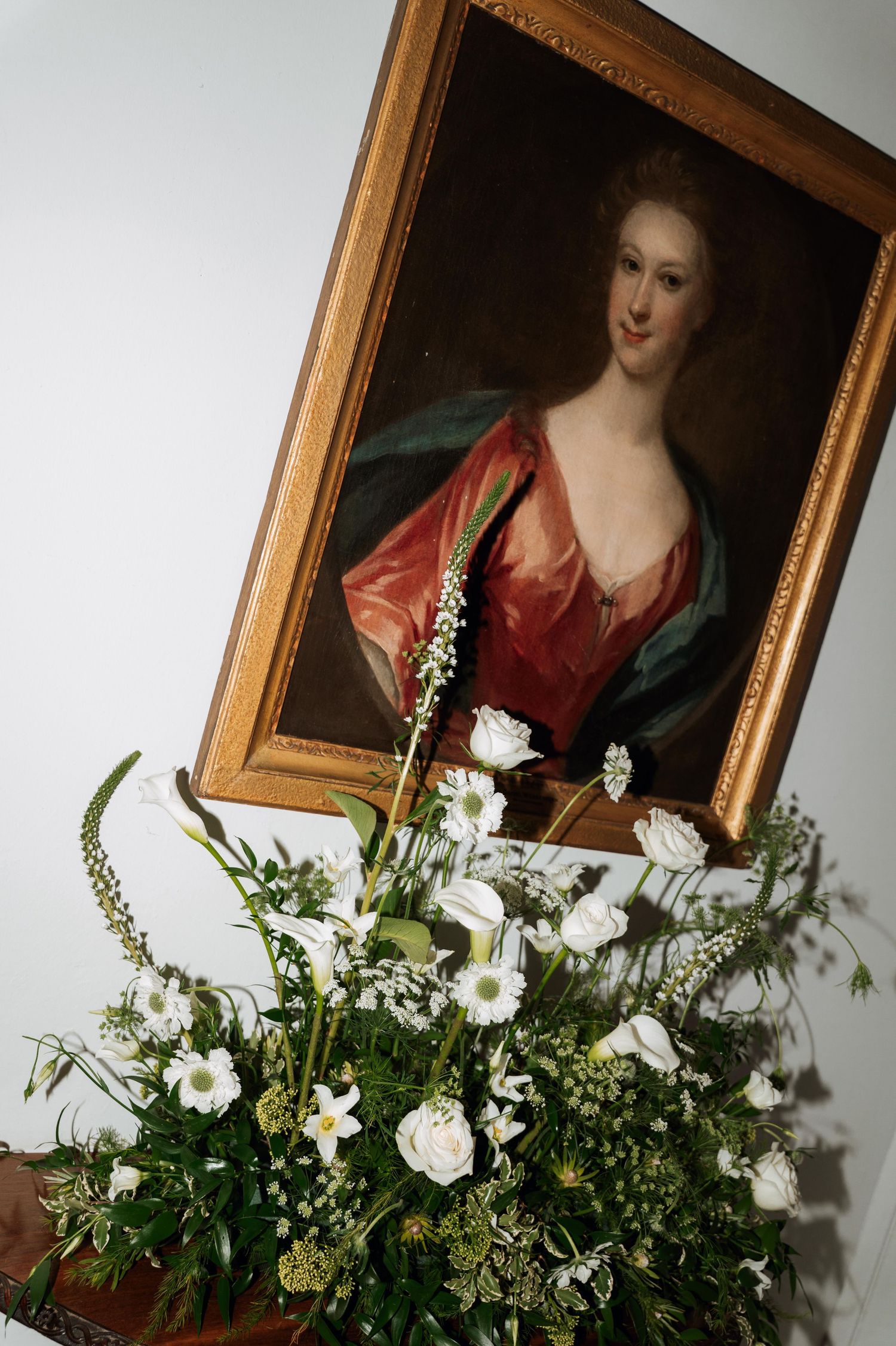 Fresh white floral arrangement with greenery displayed beneath a classical portrait painting in ornate gold frame.