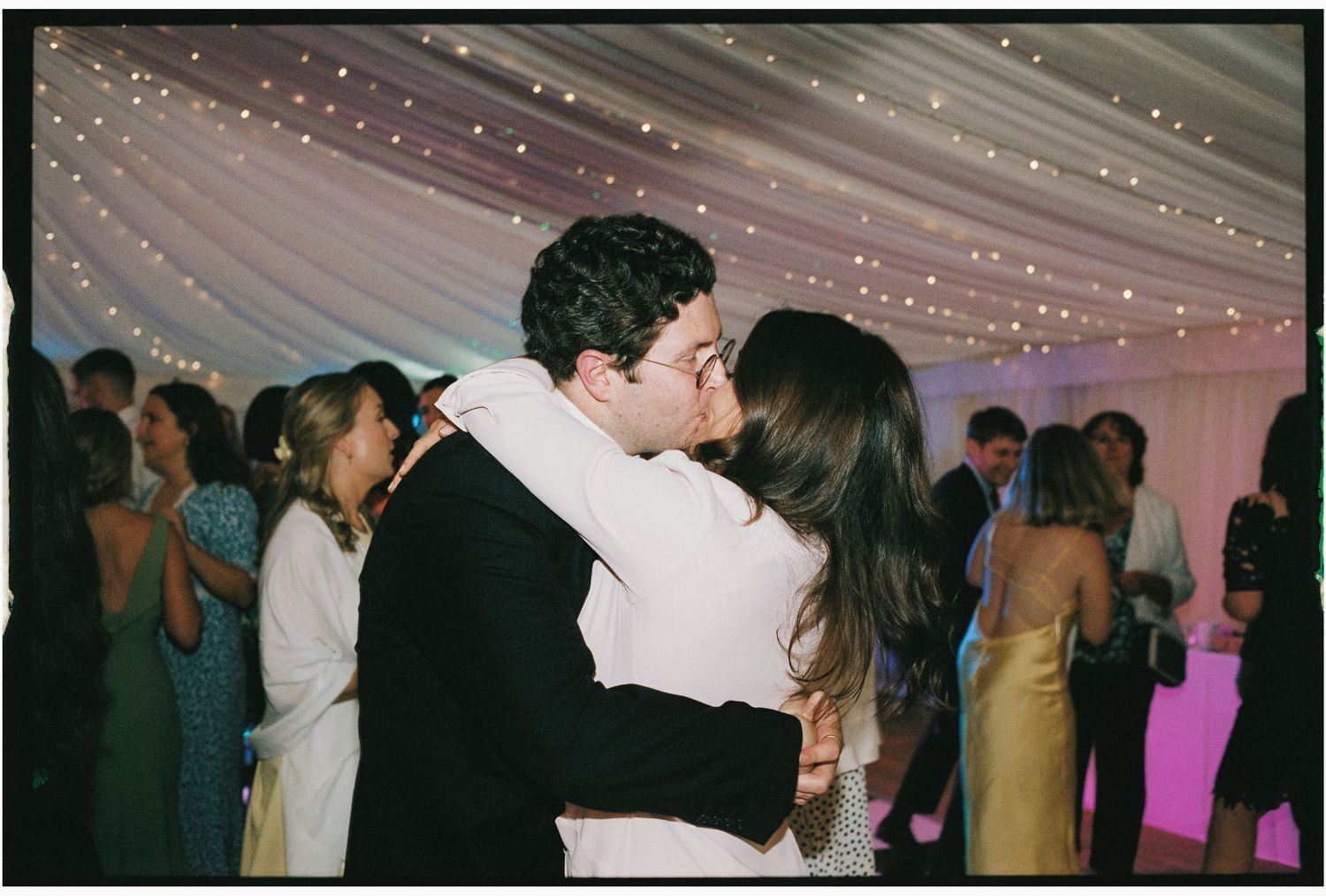 A couple shares a romantic dance moment under twinkling lights at an indoor wedding reception.