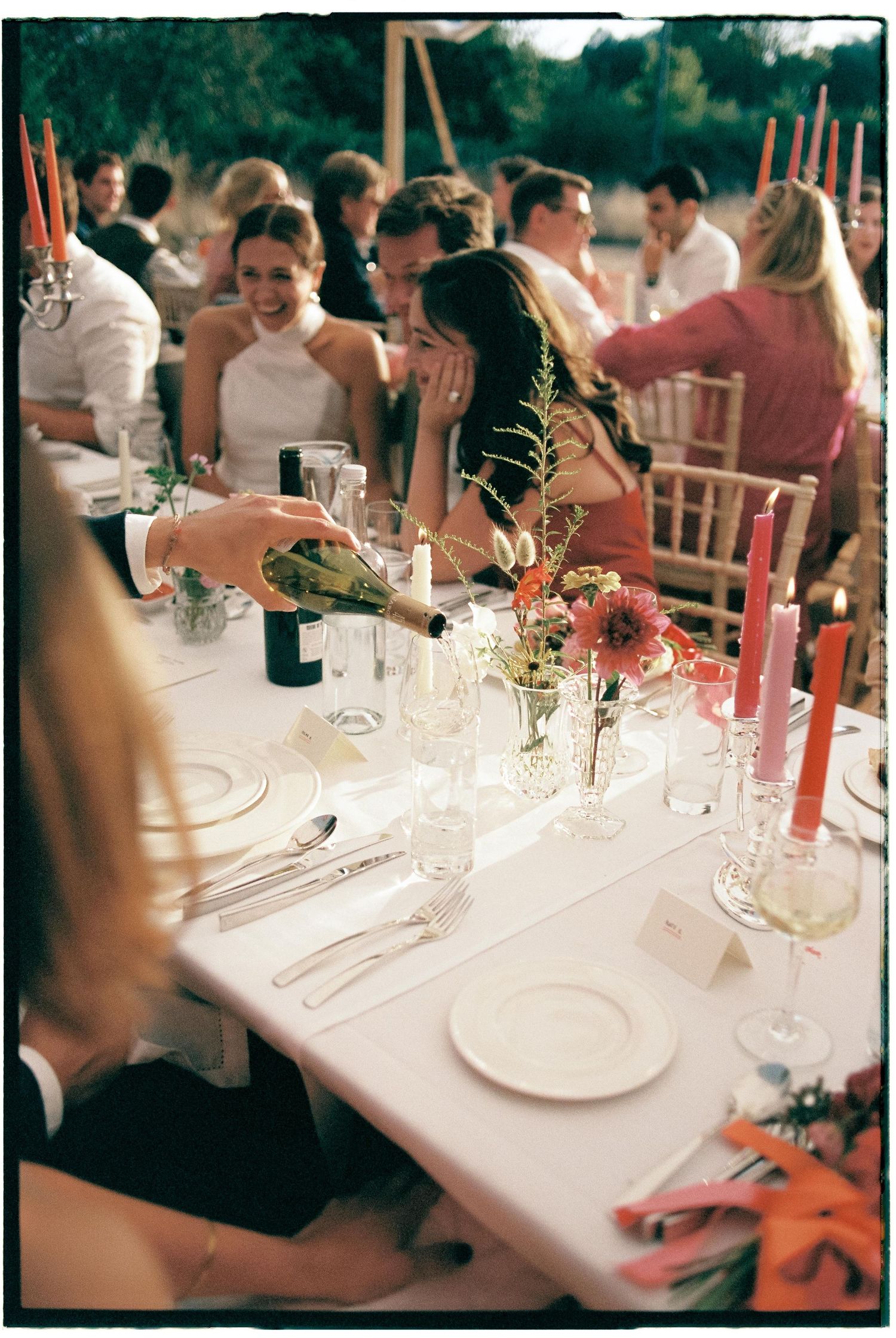 Wedding reception guests seated at elegant white-clothed dining tables with floral centerpieces and formal place settings.