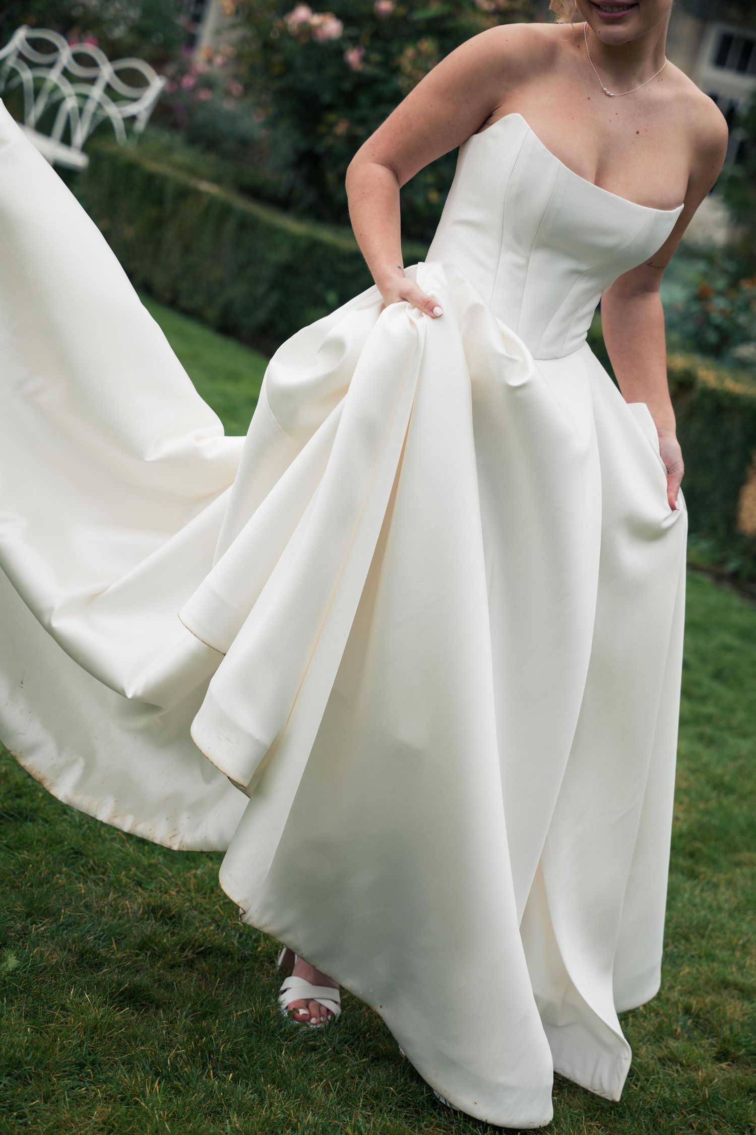 A flowing white wedding dress is shown in motion as the wearer twirls gracefully on grass outdoors.