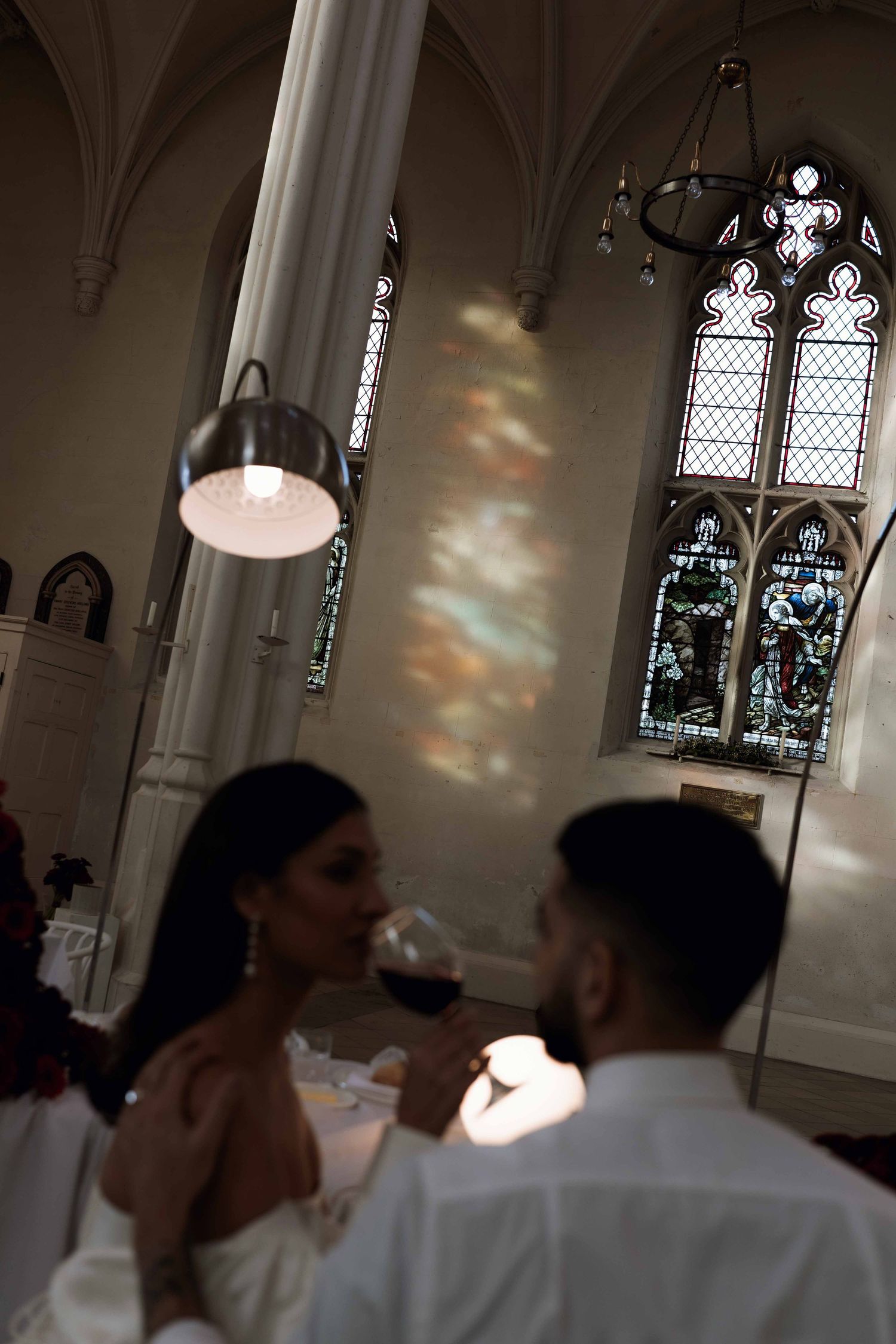 Stained glass windows and gothic architecture frame a romantic wedding reception scene in a church.