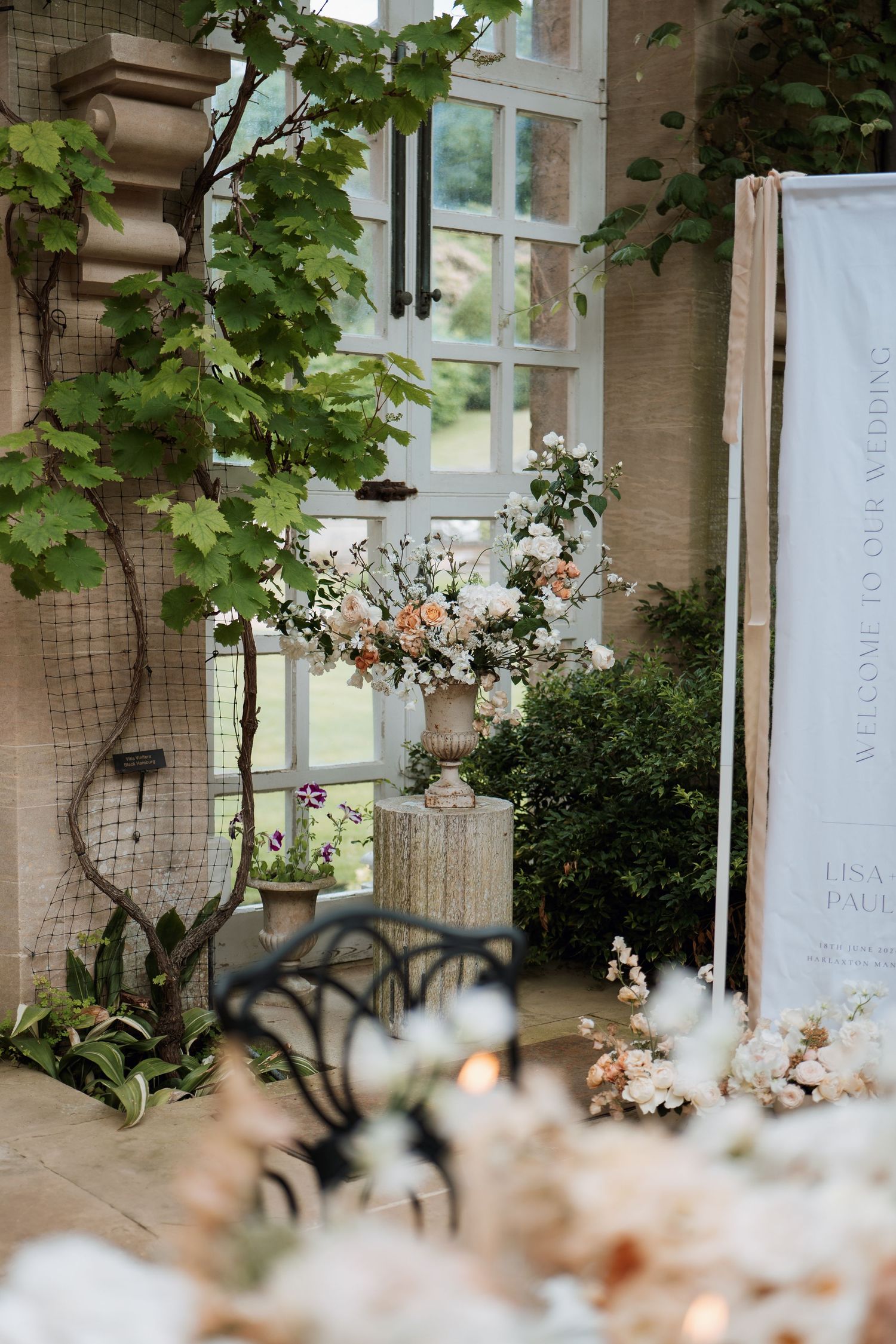 A vintage window with climbing vines and delicate flowers creates a romantic garden scene with soft natural lighting at Harlaxton Manor.