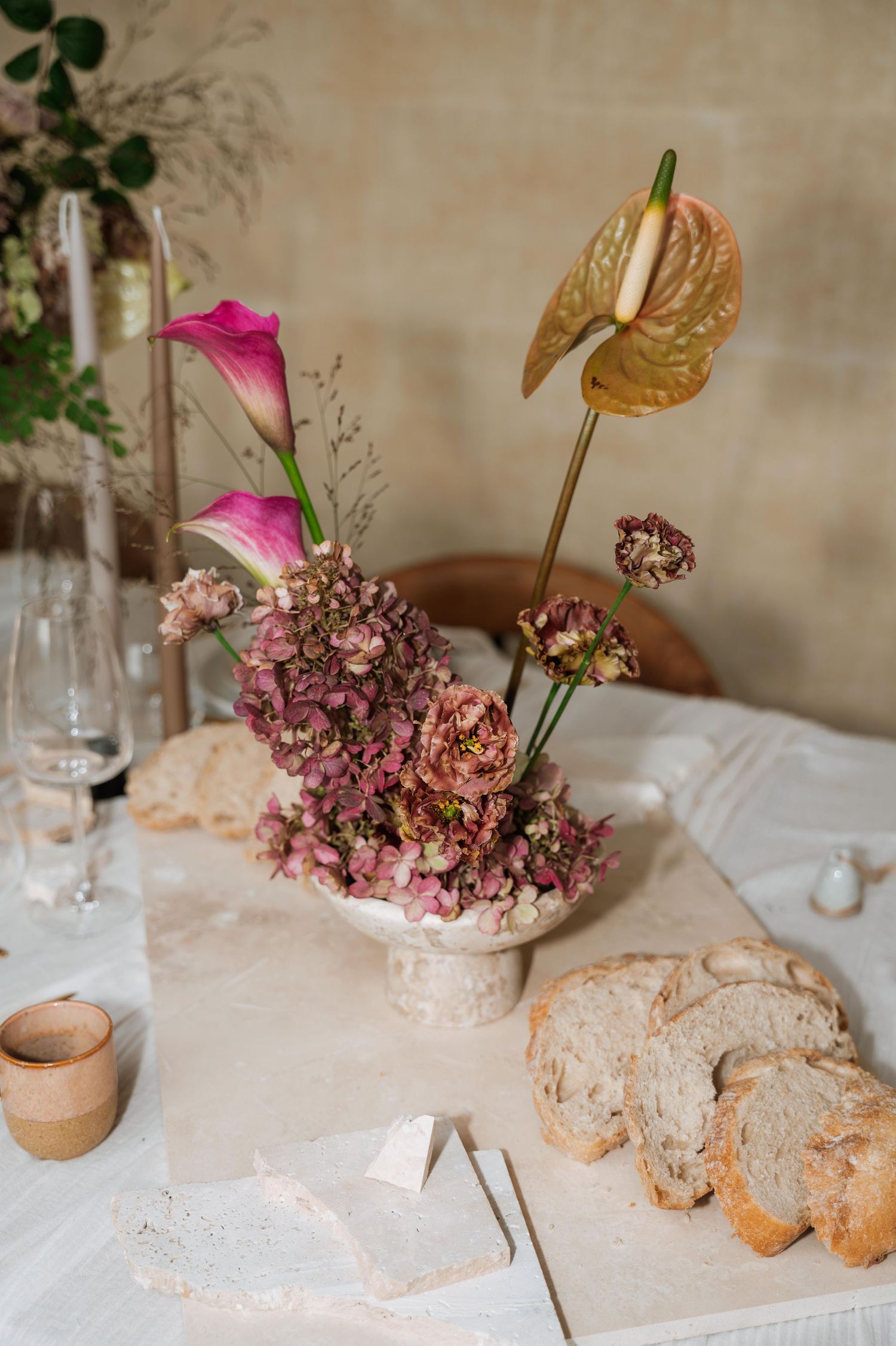 Elegant table setting with dried pink hydrangeas, gold accents, and rustic bread on a white tablecloth.