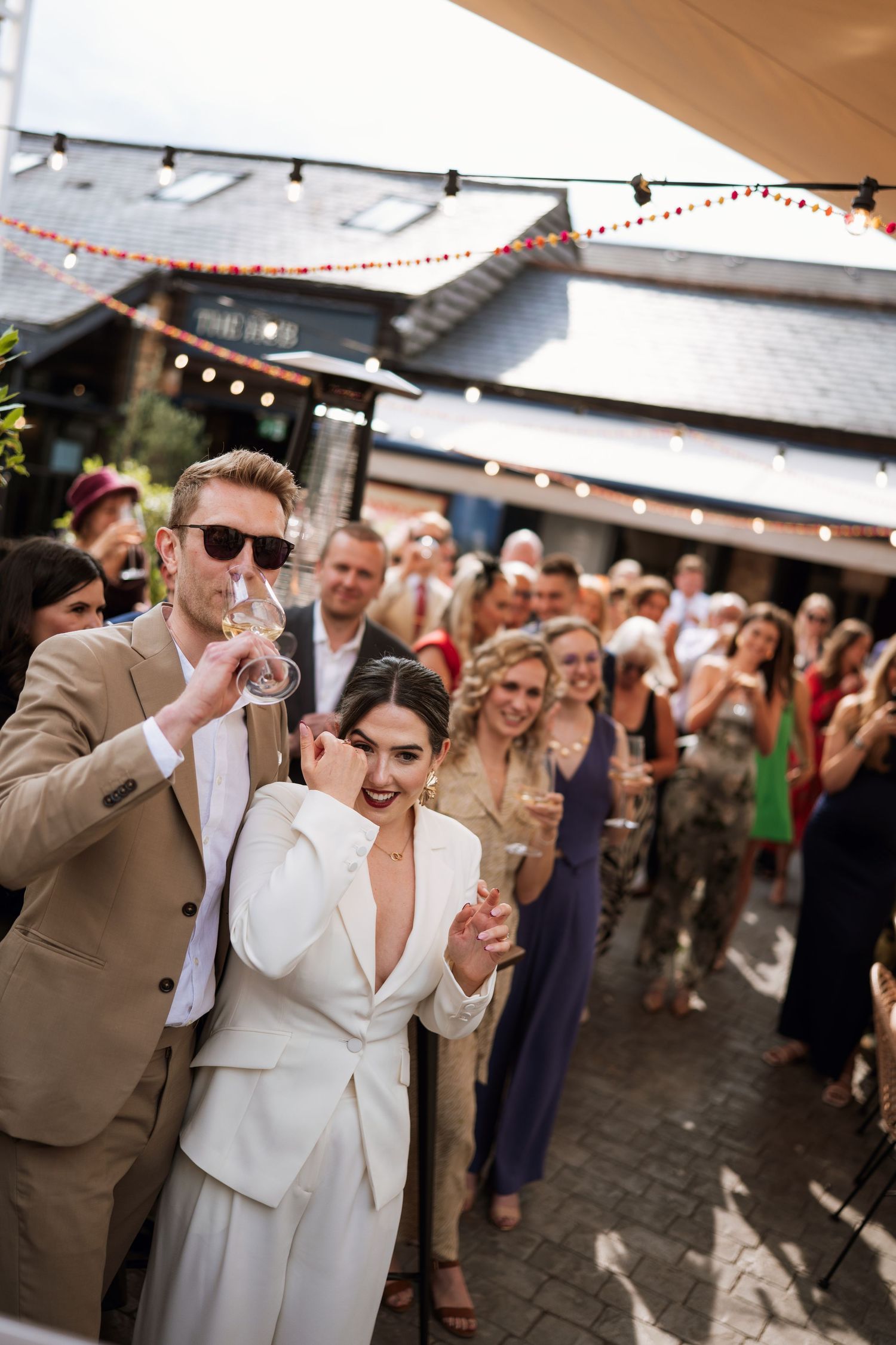 Wedding couple dances joyfully on an outdoor patio as guests cheer and celebrate during a festive reception.