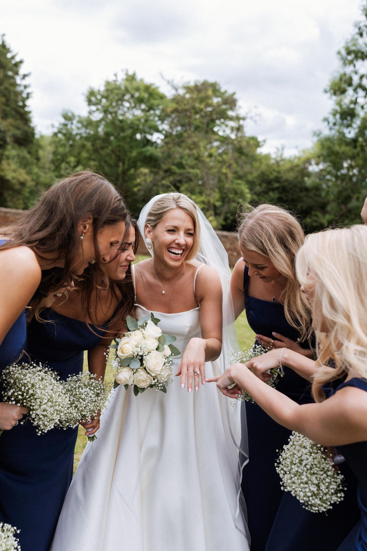A joyful wedding party in navy blue and white dresses laughs together in a candid outdoor photo series.