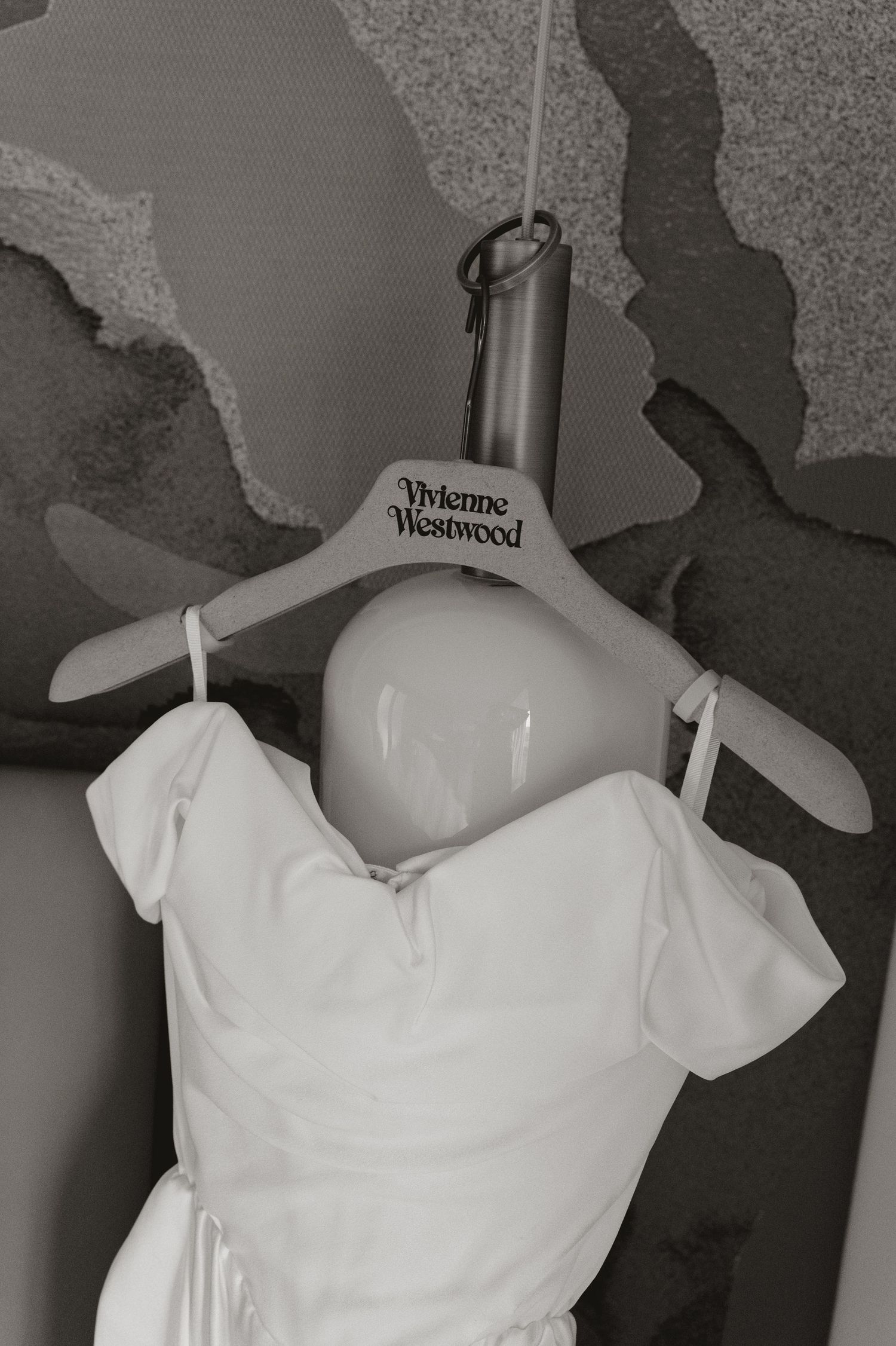 A white Vivienne Westwood dress hangs on display, showcasing its classic design and elegant off-shoulder neckline.