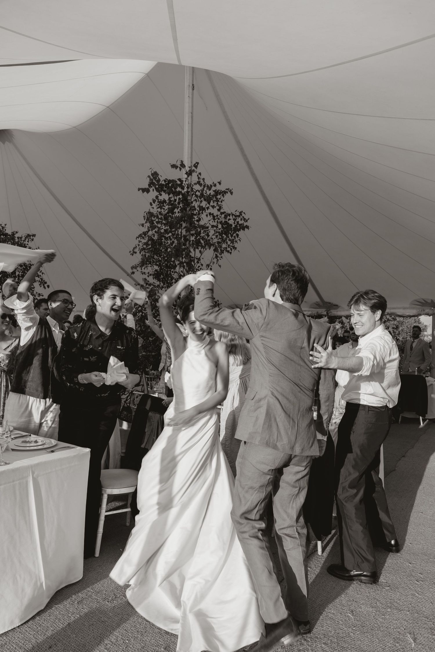 Couples dancing and celebrating at an outdoor wedding reception under a white tent canopy.