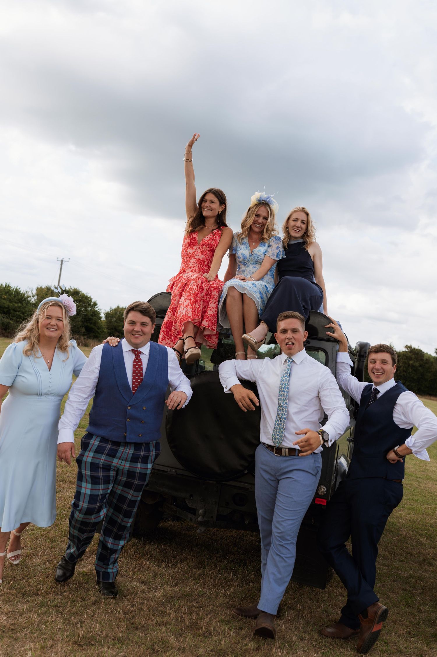 A group of friends pose together on a large tractor tire in a field under cloudy skies.
