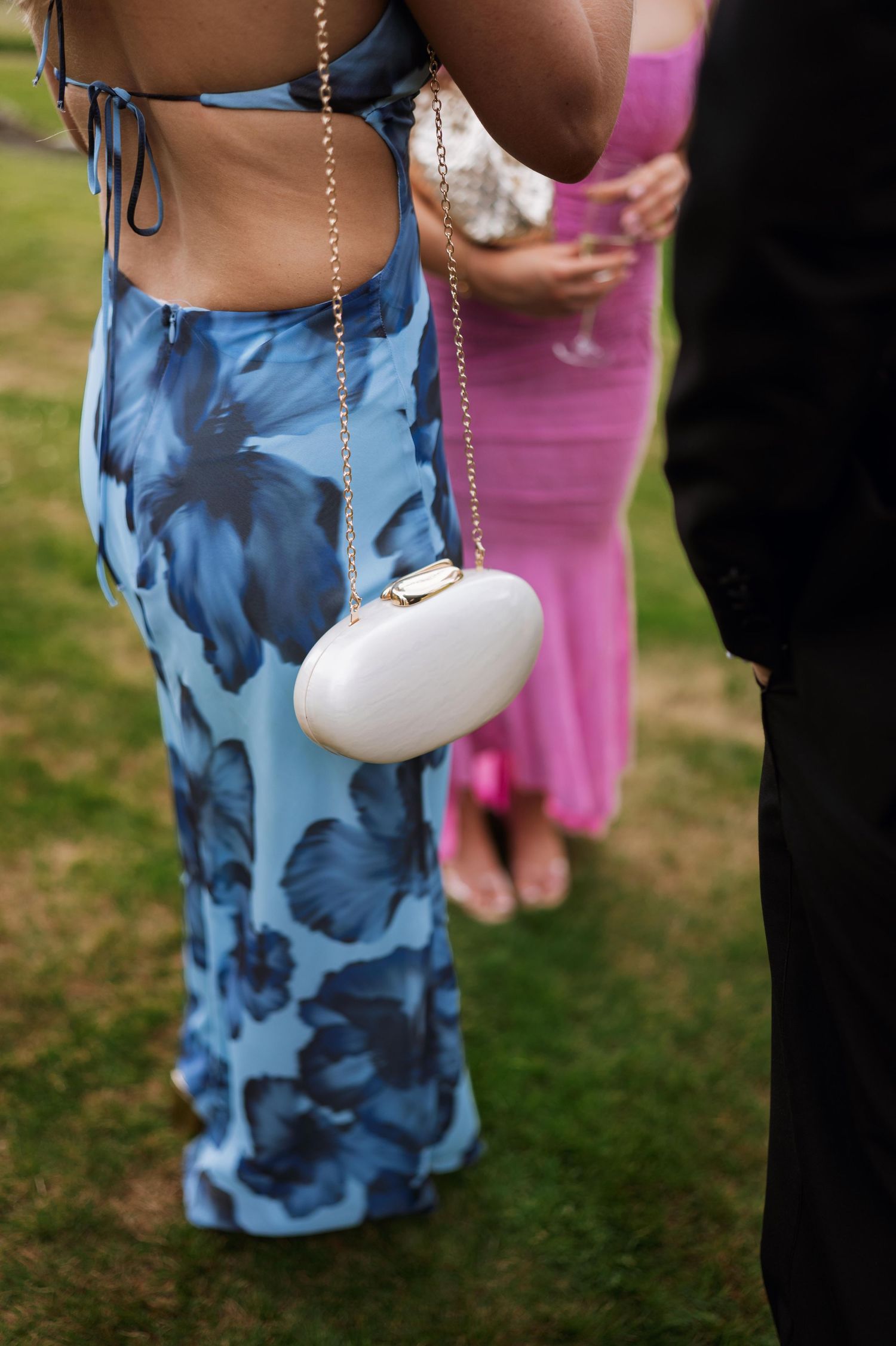 A person wearing blue floral patterned clothing holds a small white purse on a chain at an outdoor event.