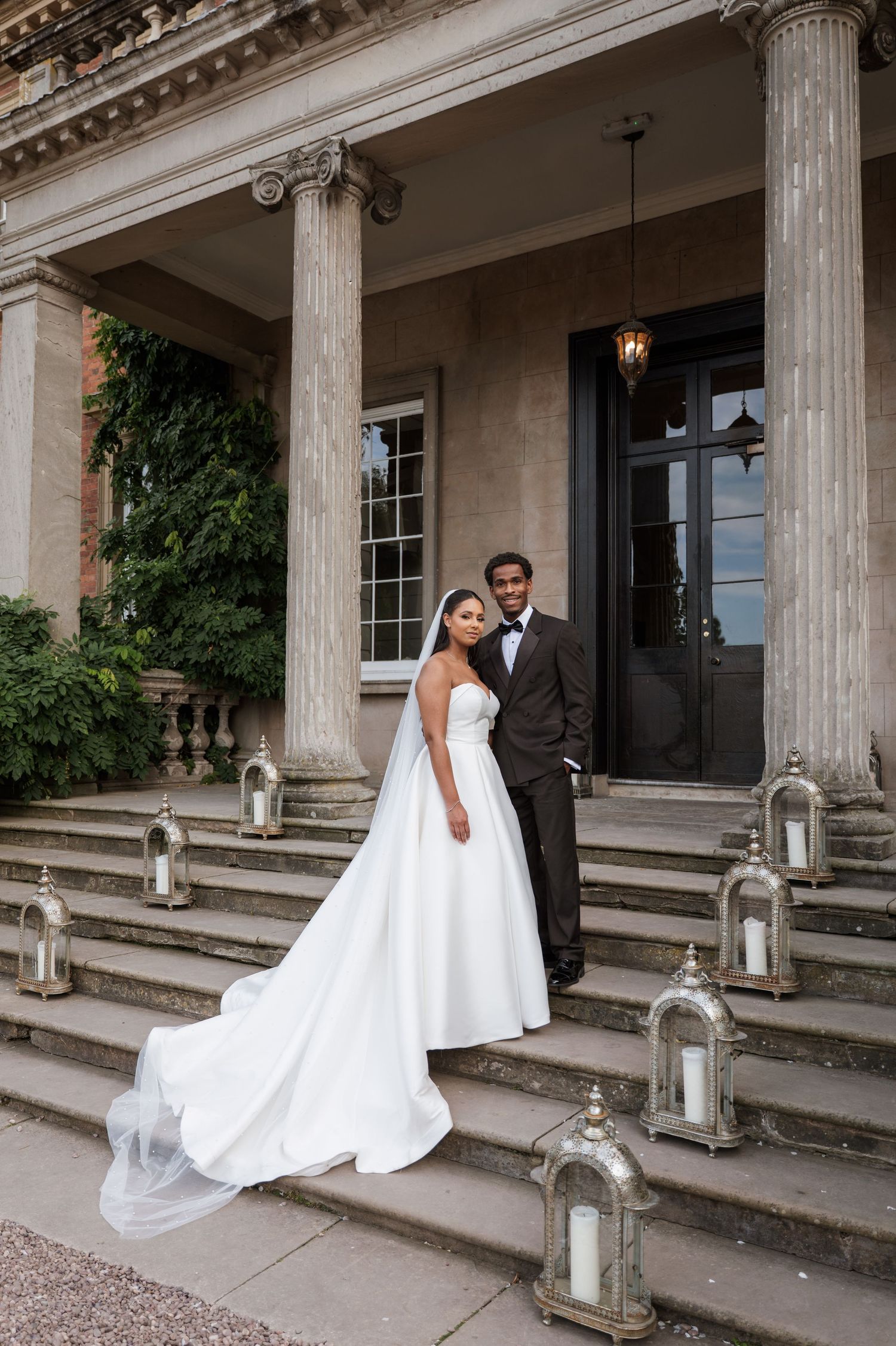 A romantic wedding couple shares intimate moments on the steps of a grand columned building with decorative lanterns.