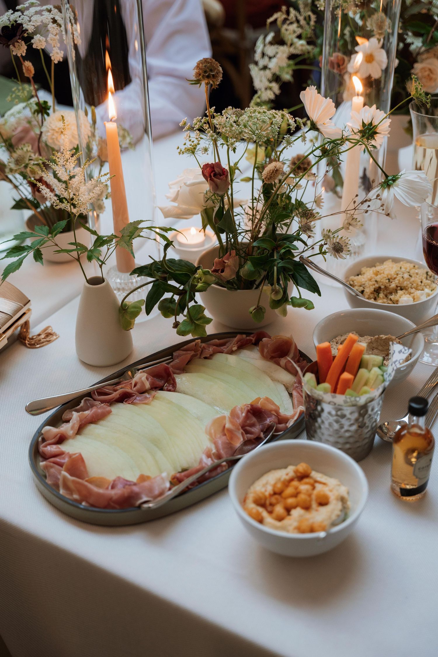 Elegant table setting with charcuterie boards, floral arrangements and candles on white tablecloth at upscale event.
