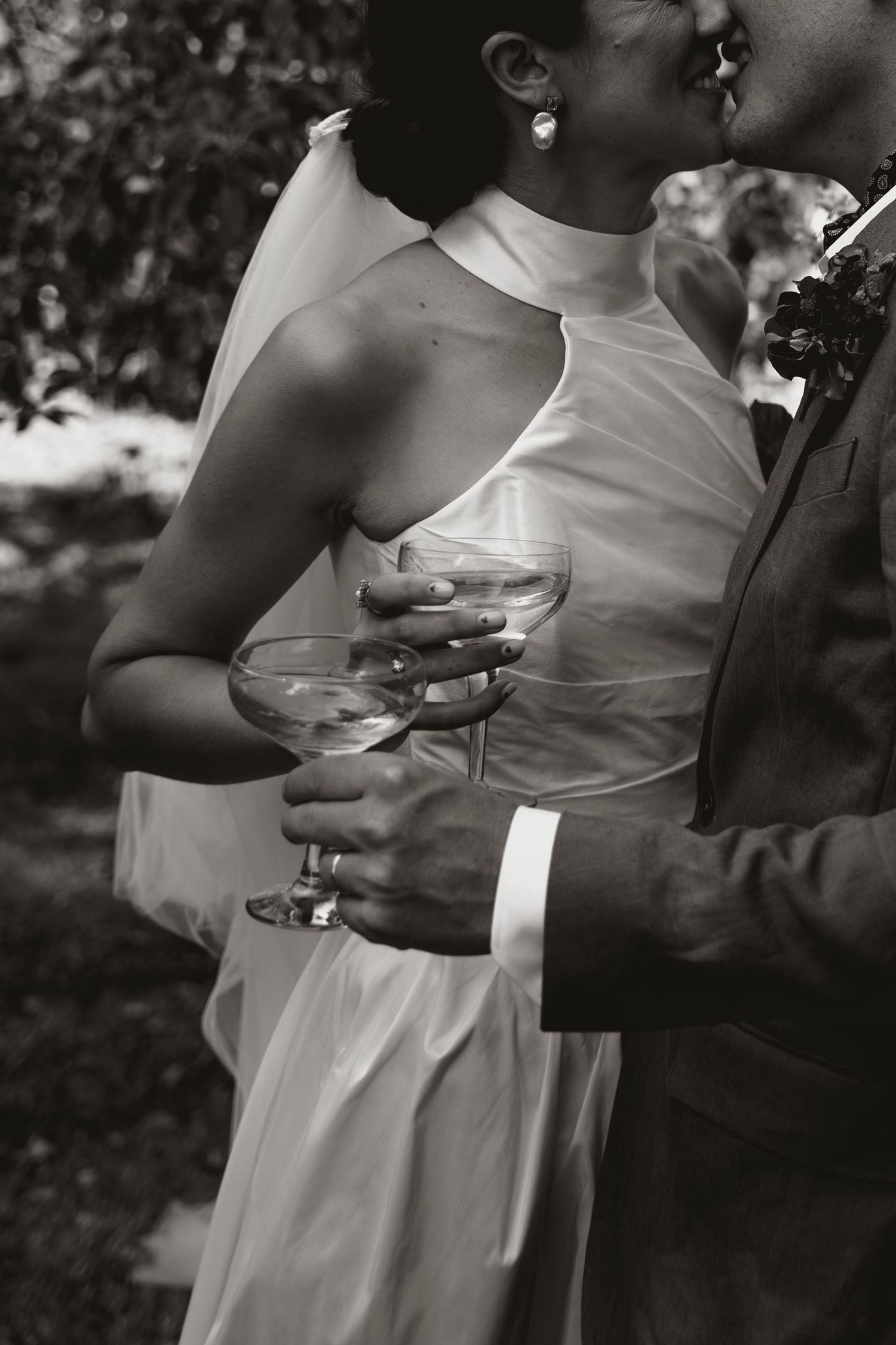 A romantic black and white wedding photo showing a couple sharing champagne glasses and an intimate moment outdoors.