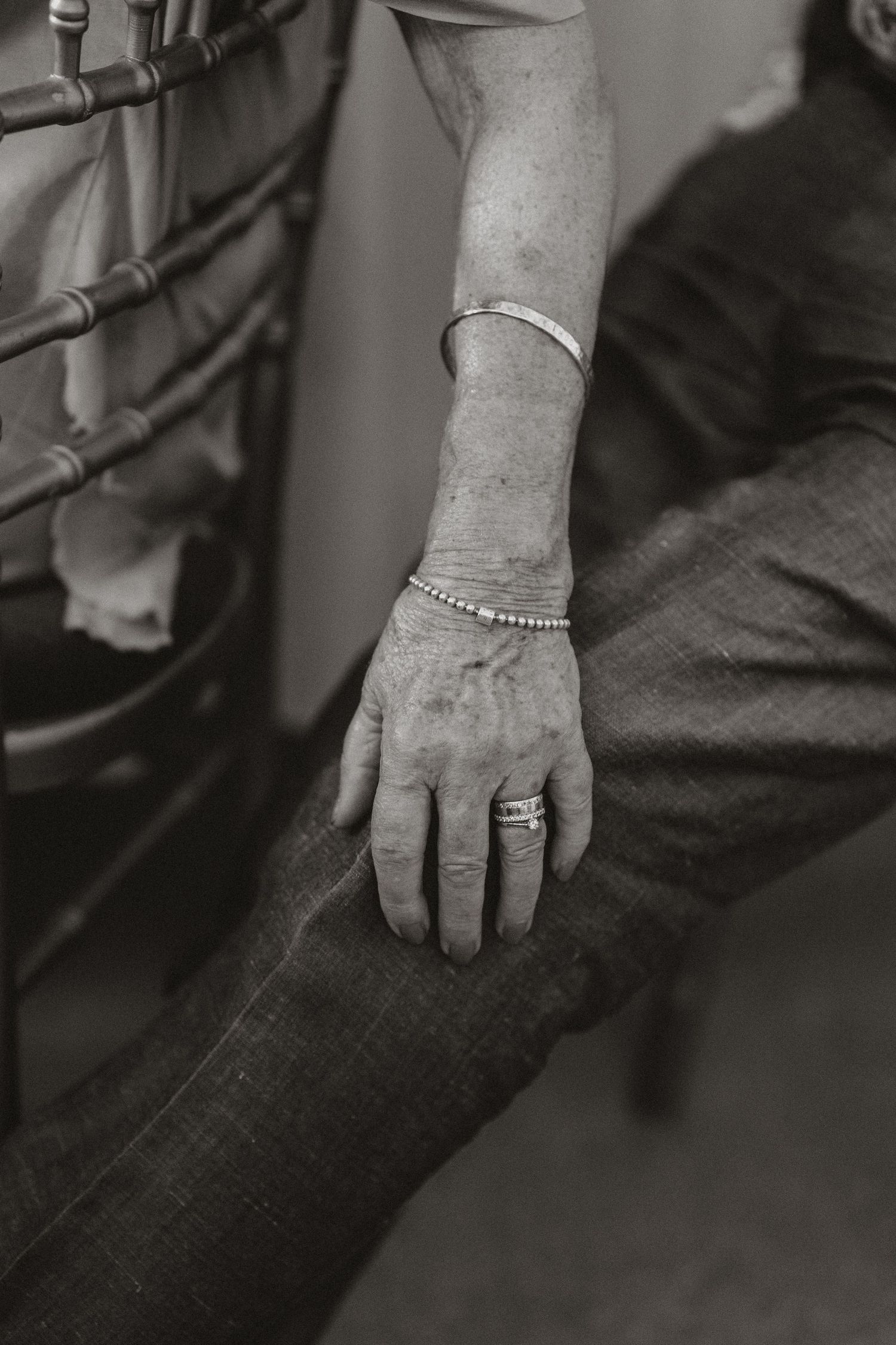 Black and white close-up photograph of a hand wearing delicate bracelets and rings resting on denim.