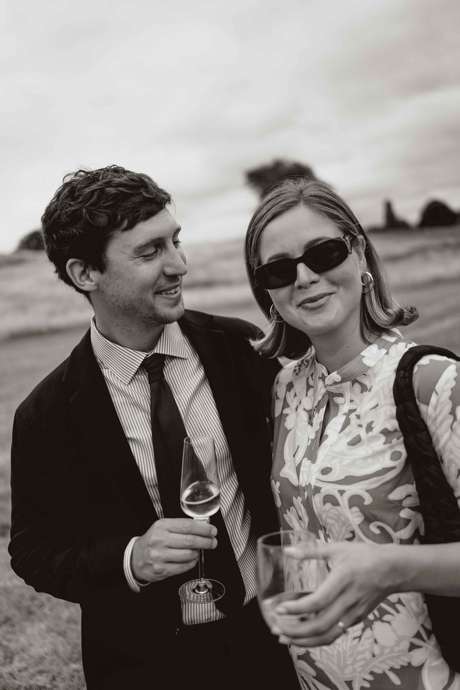 A couple in wedding attire share intimate moments in black and white photos while holding wine glasses outdoors.