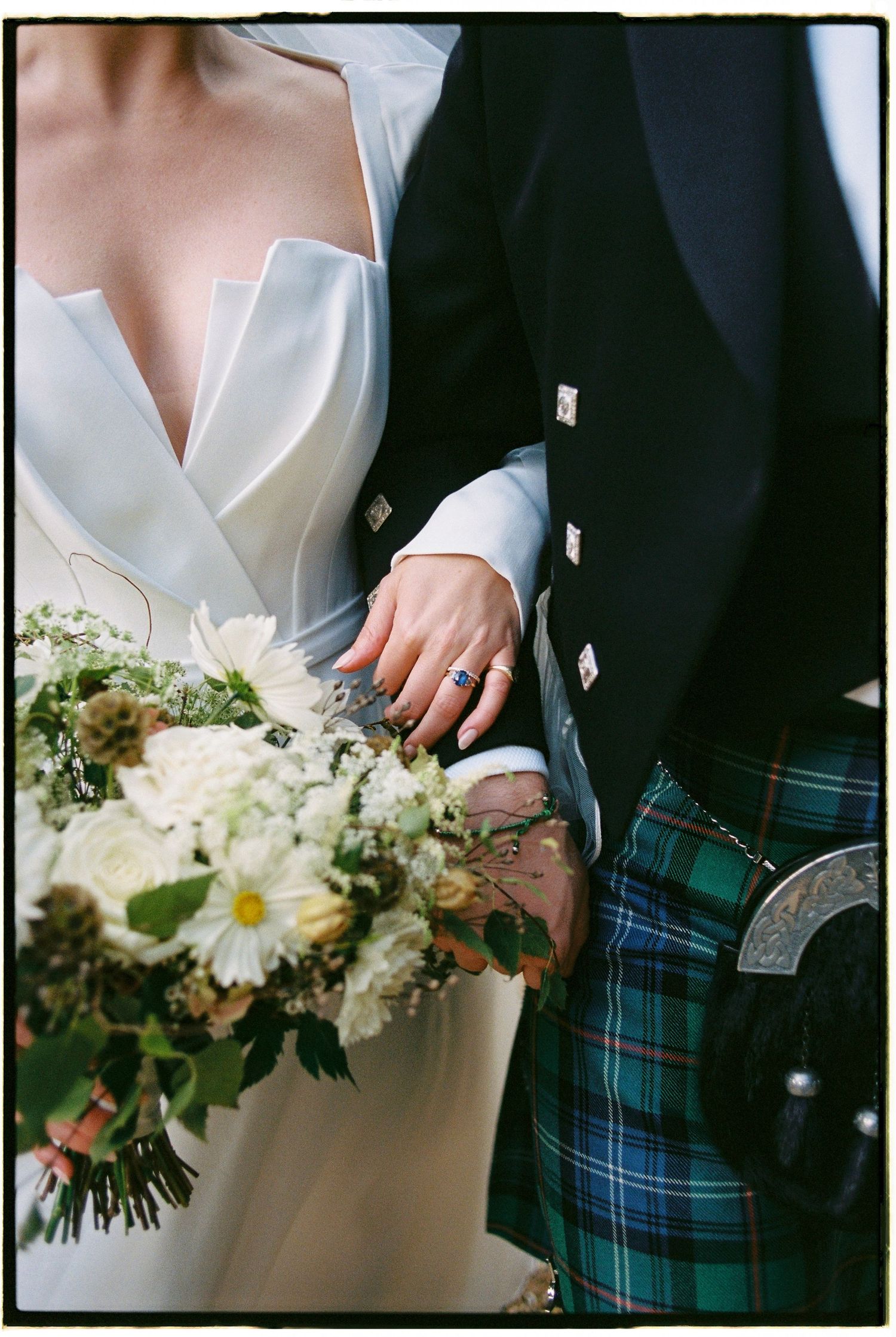 Close-up details of wedding attire showing white dress fabric and traditional blue tartan kilt at formal ceremony.