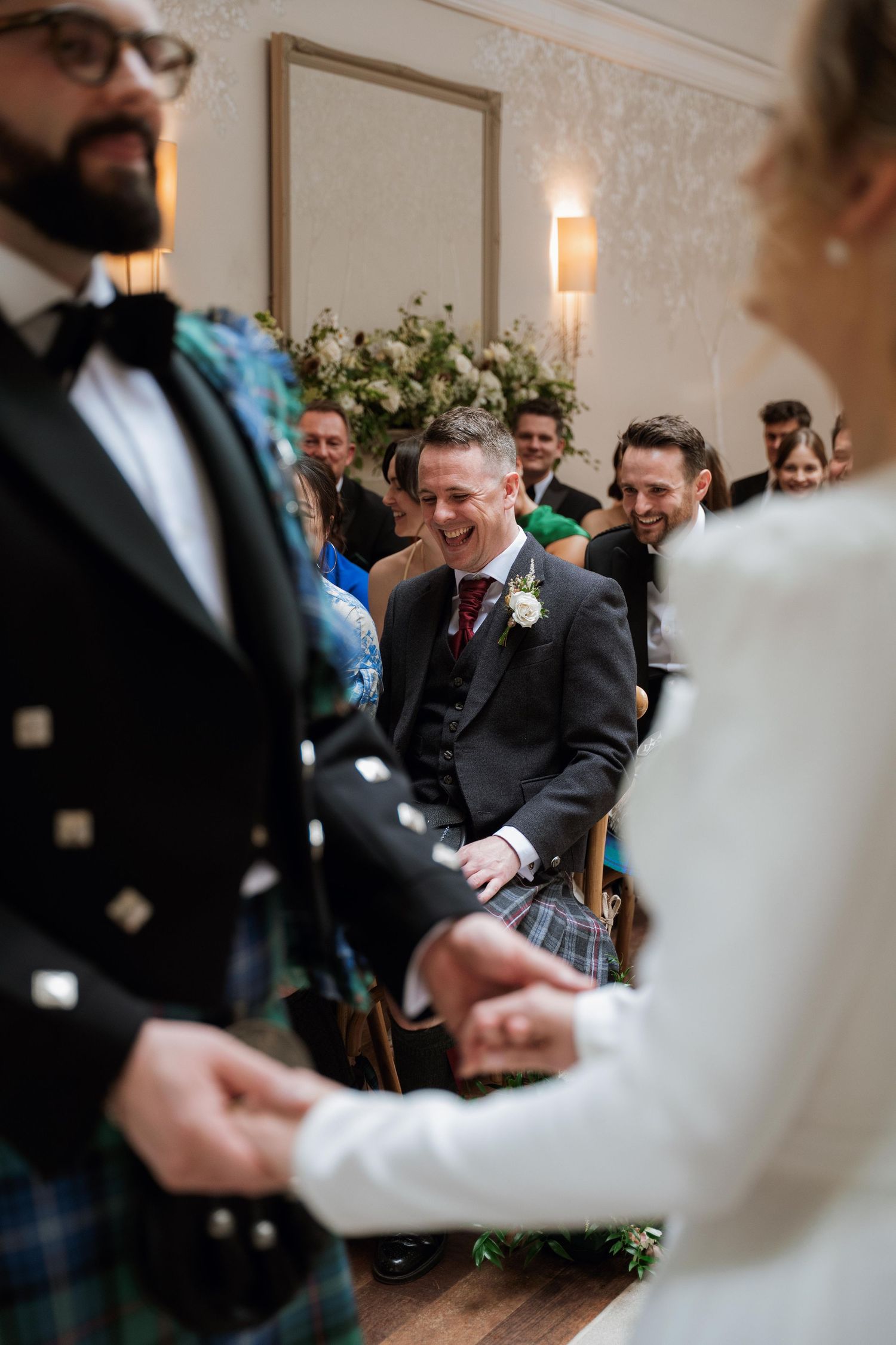 Wedding guests laugh and celebrate during a joyful moment at an indoor reception venue.
