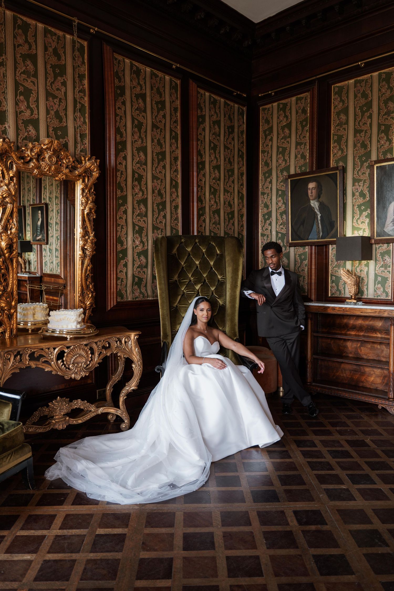 A wedding couple poses elegantly in a vintage room with ornate wallpaper and parquet flooring.