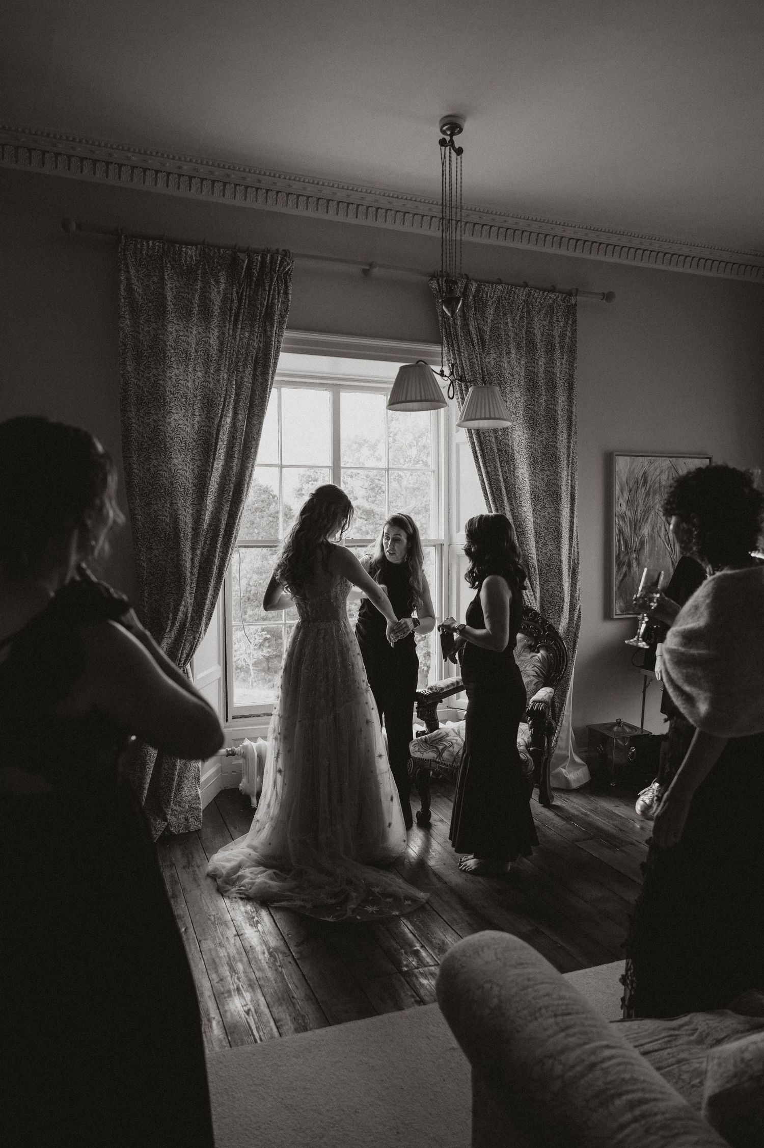 Black and white photo series showing preparations for a wedding with a bride in a flowing gown and attendants in a sunlit room.