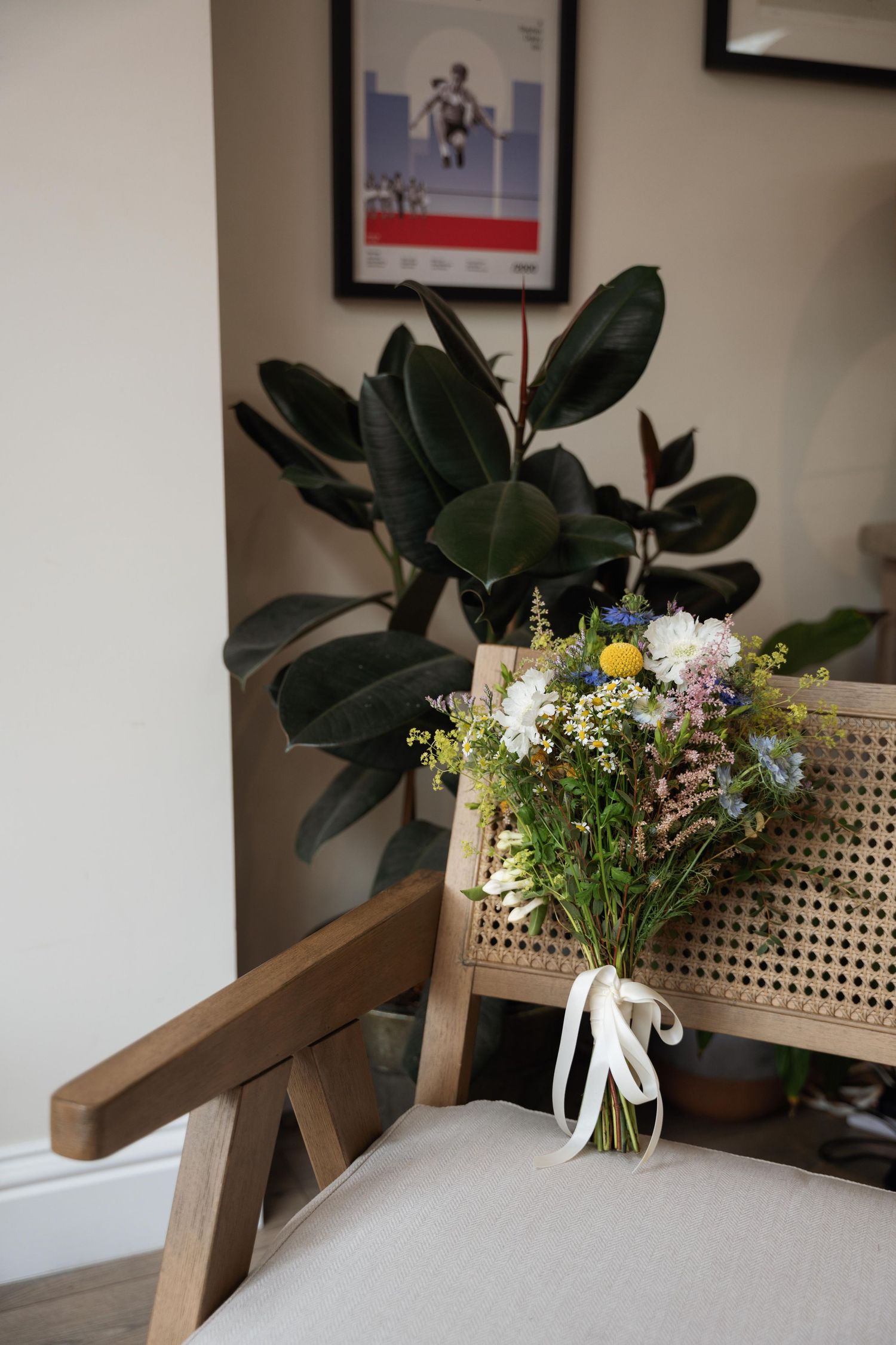 A wooden bench with a decorative vase of fresh wildflowers sits against a white wall with a fiddle leaf fig plant.