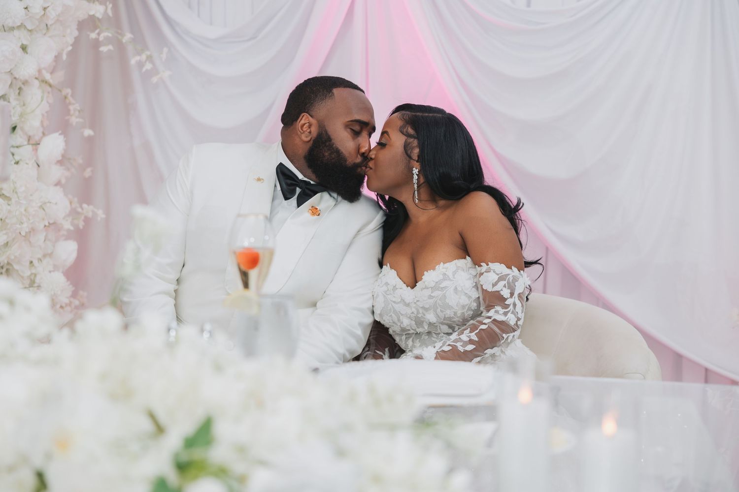 A couple shares an intimate moment at their wedding reception surrounded by white decor and floral arrangements.