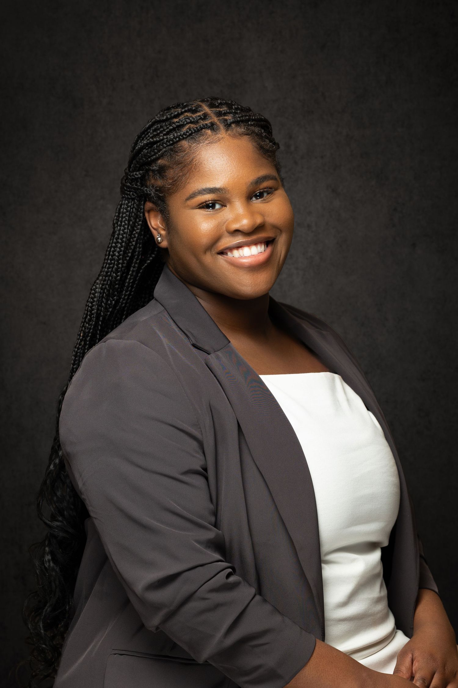 Professional portrait in studio lighting featuring a person in a dark blazer and white top against a textured dark background.