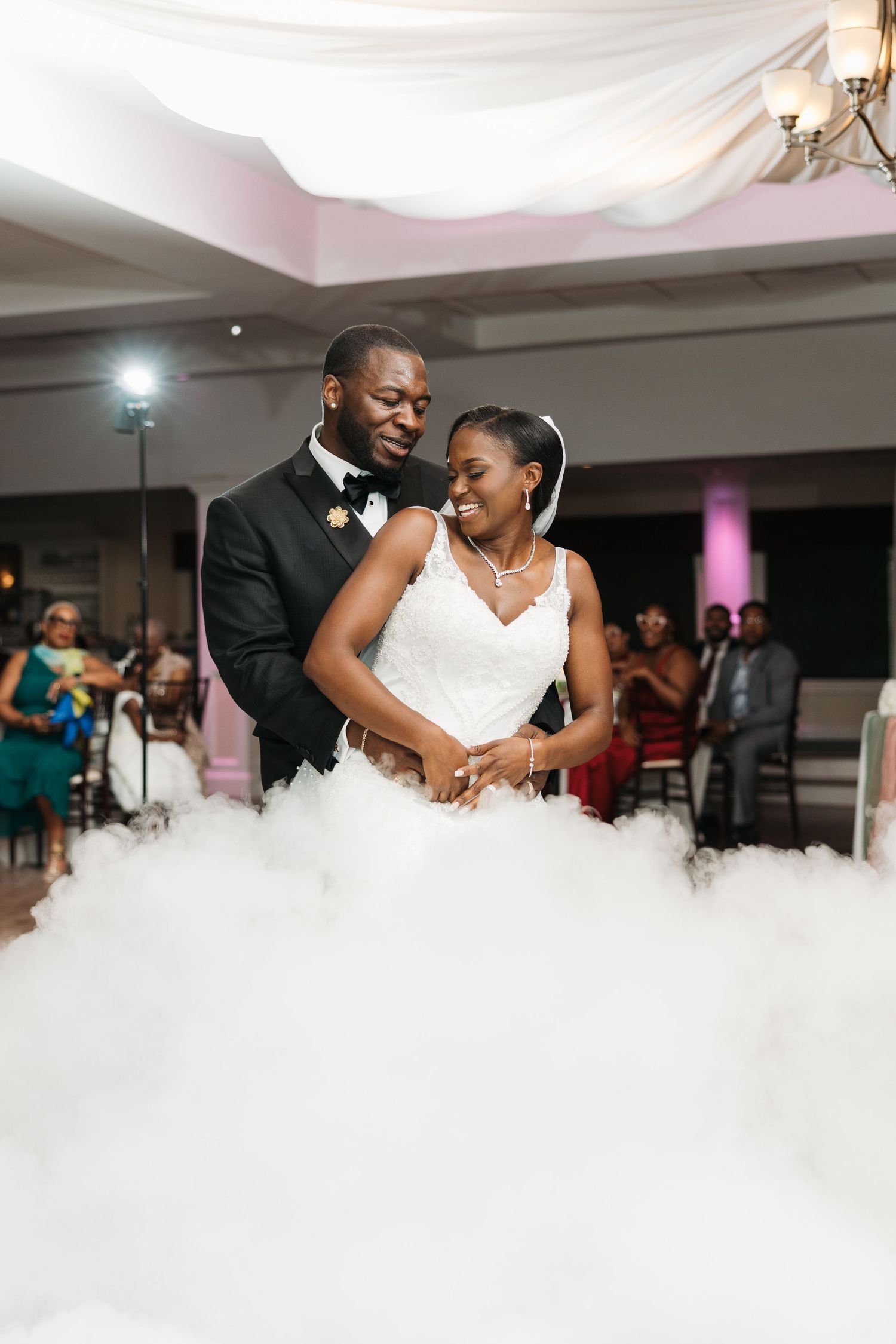 Bride and groom share first dance surrounded by dramatic fog machine clouds at elegant wedding reception.