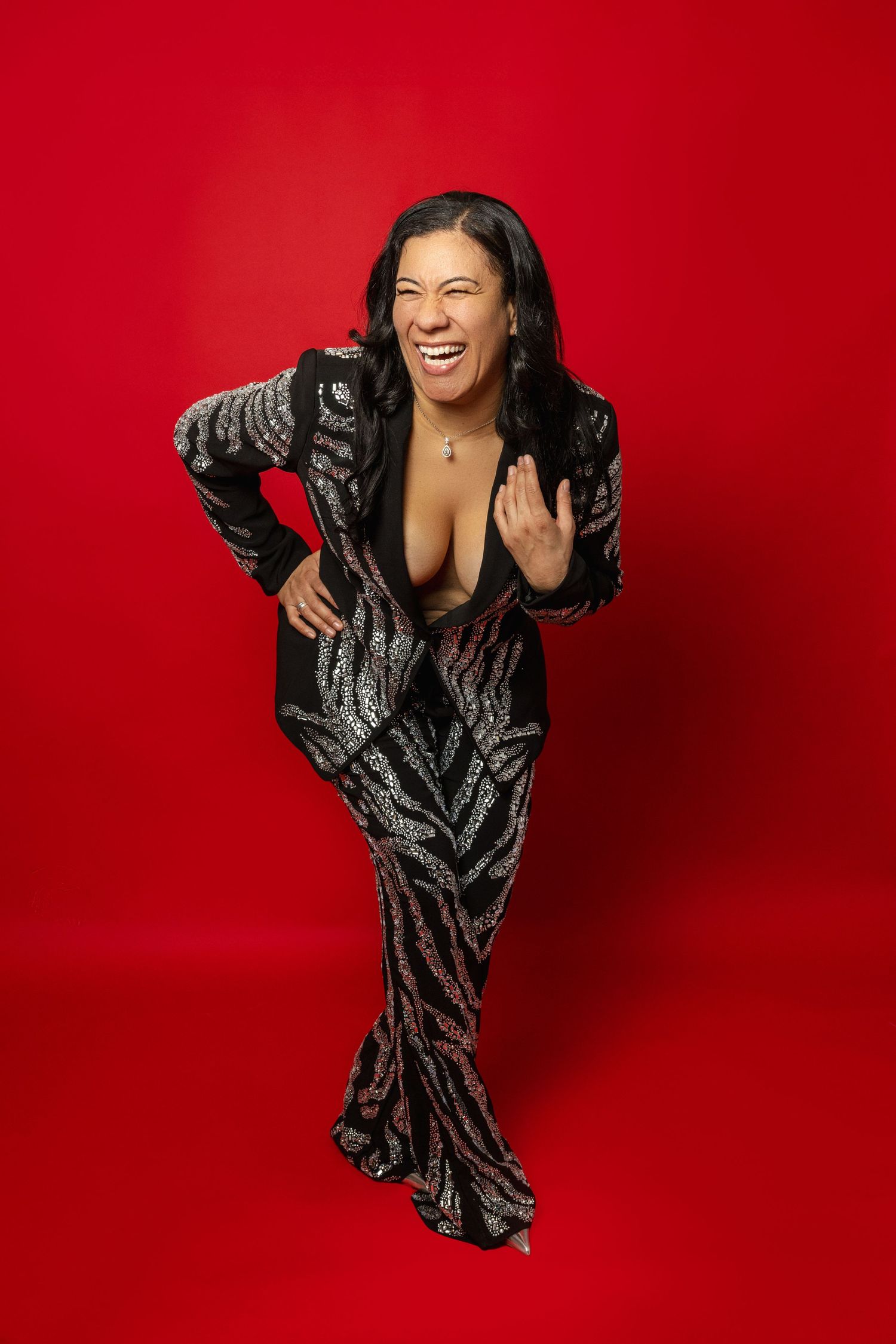 Someone wearing a sparkly black and silver evening gown poses joyfully against a bright red background.
