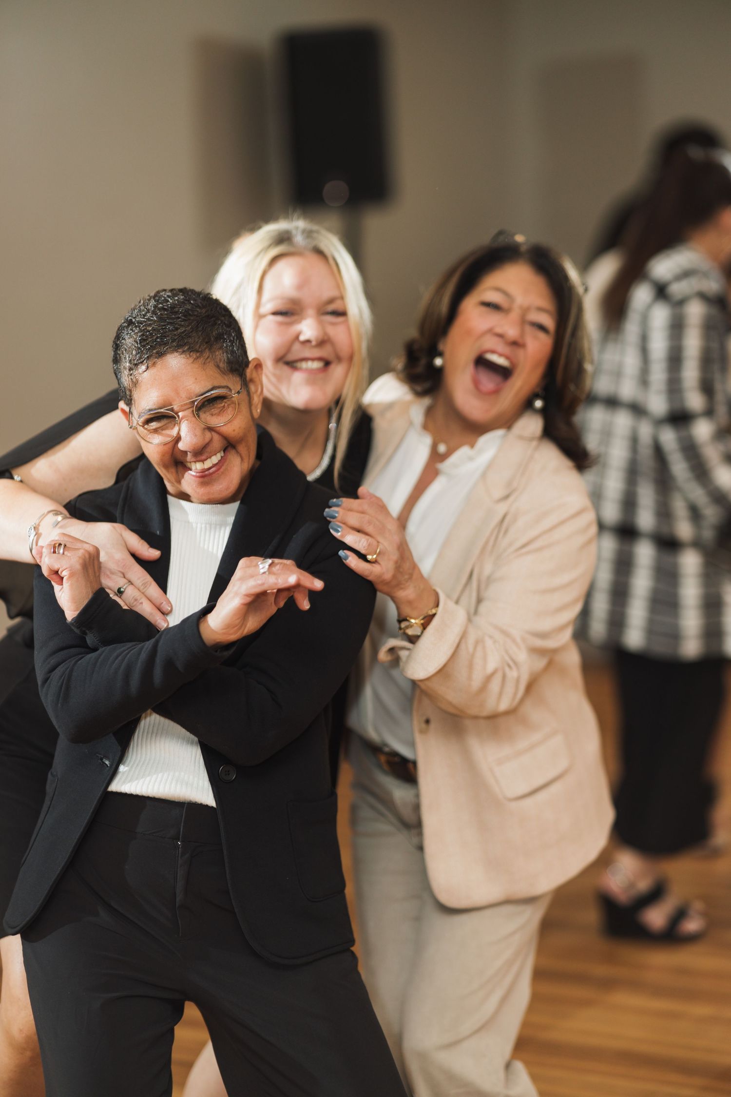 A group of people dancing and laughing together with joyful expressions in a dance studio with wooden floors.