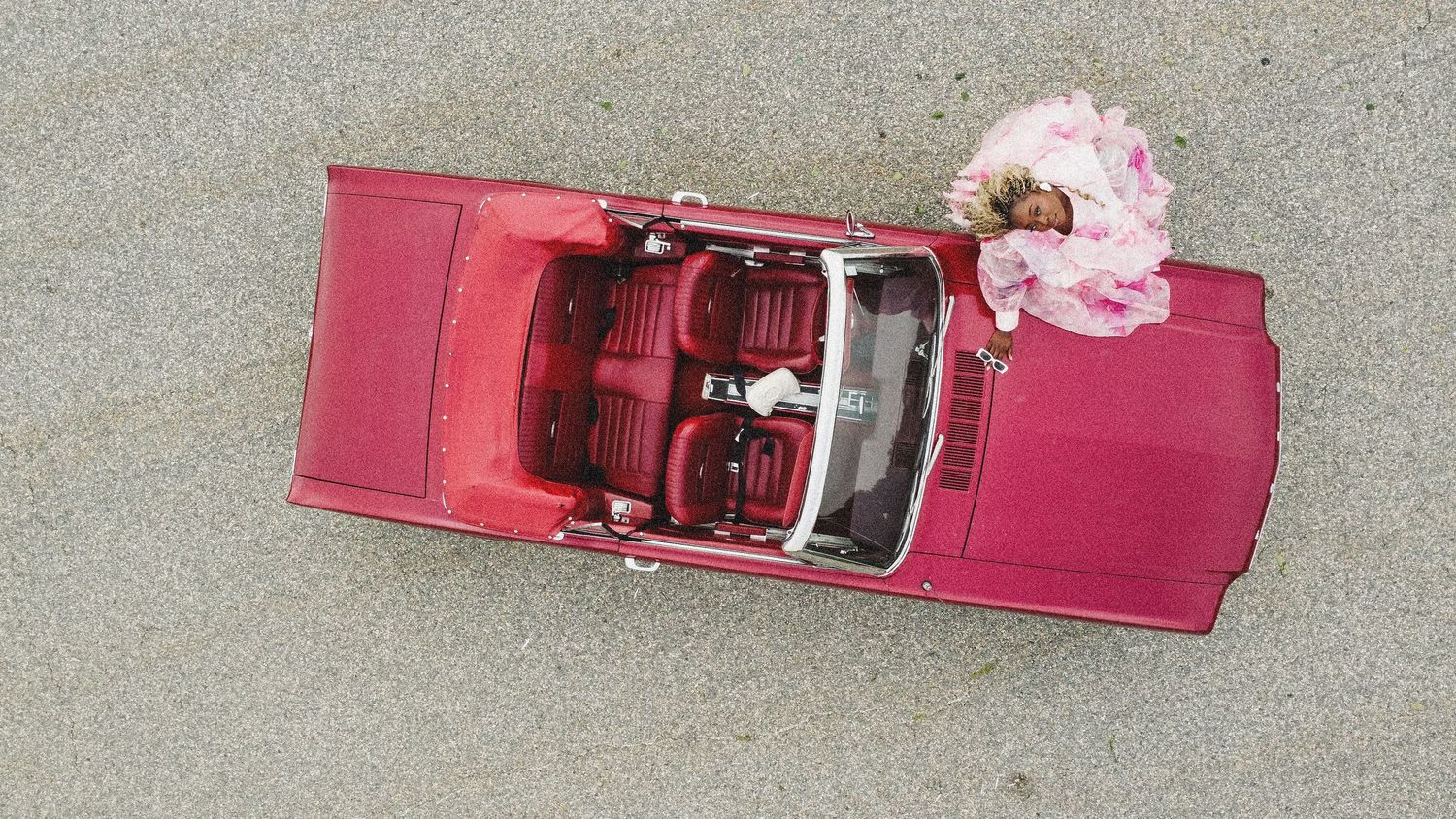 Pink Cadillac convertible photographed from above with decorated trunk or back seat, parked on concrete surface.