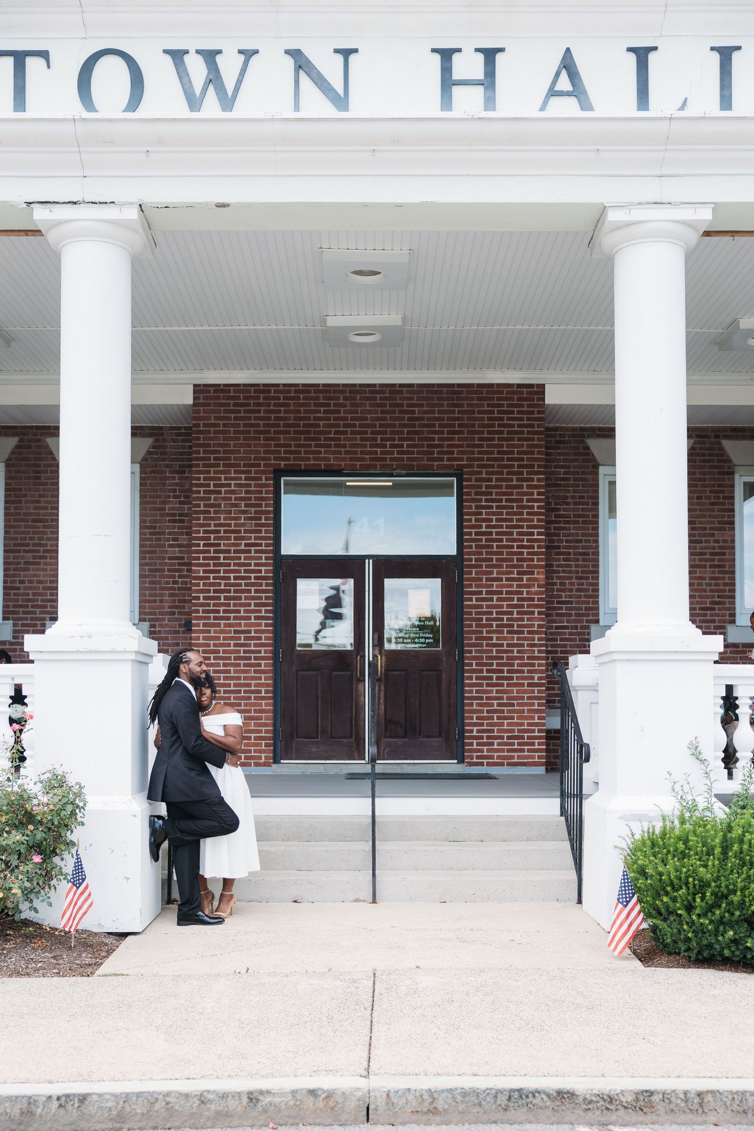 A red brick town hall building with white columns and an American flag displayed near the entrance.
