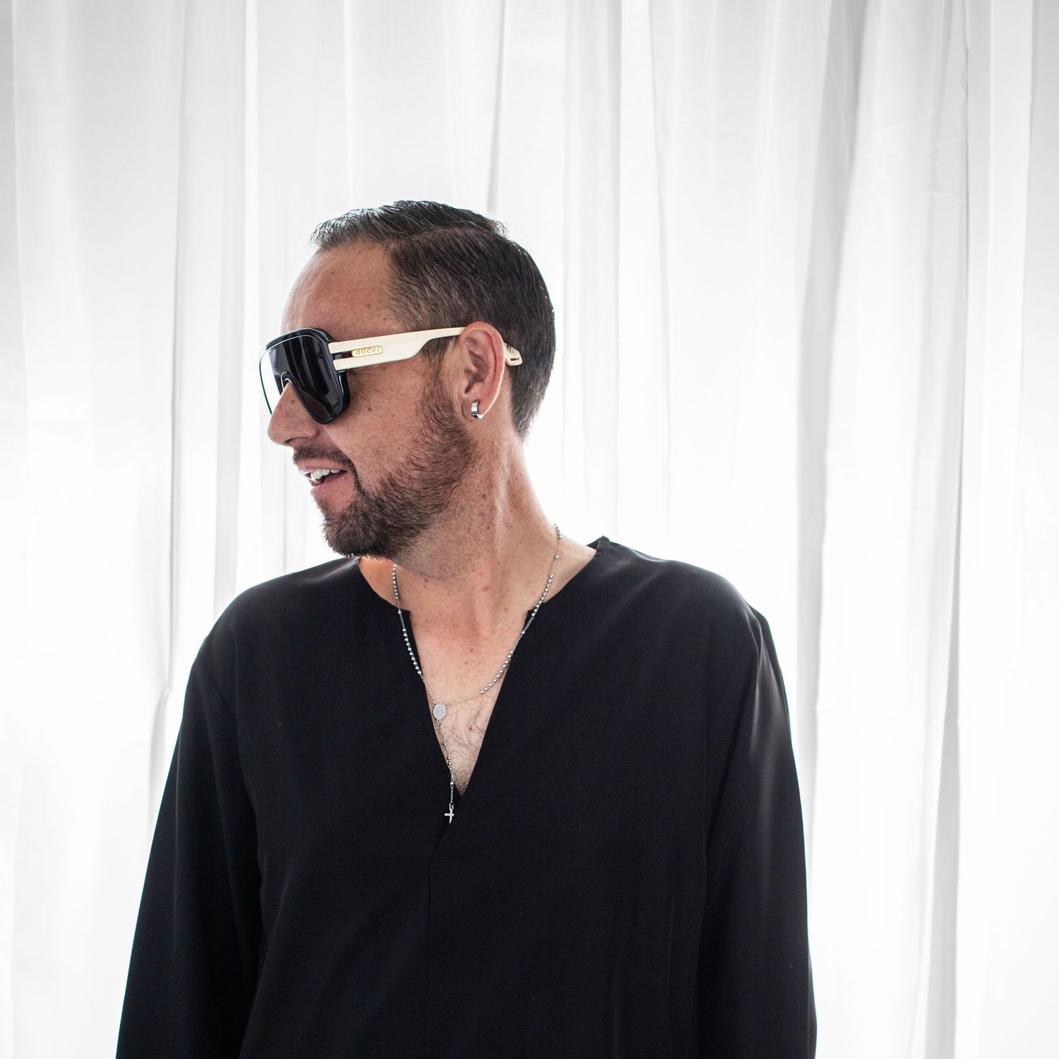 Person wearing sunglasses and dark clothing stands against white curtain background in three different poses.