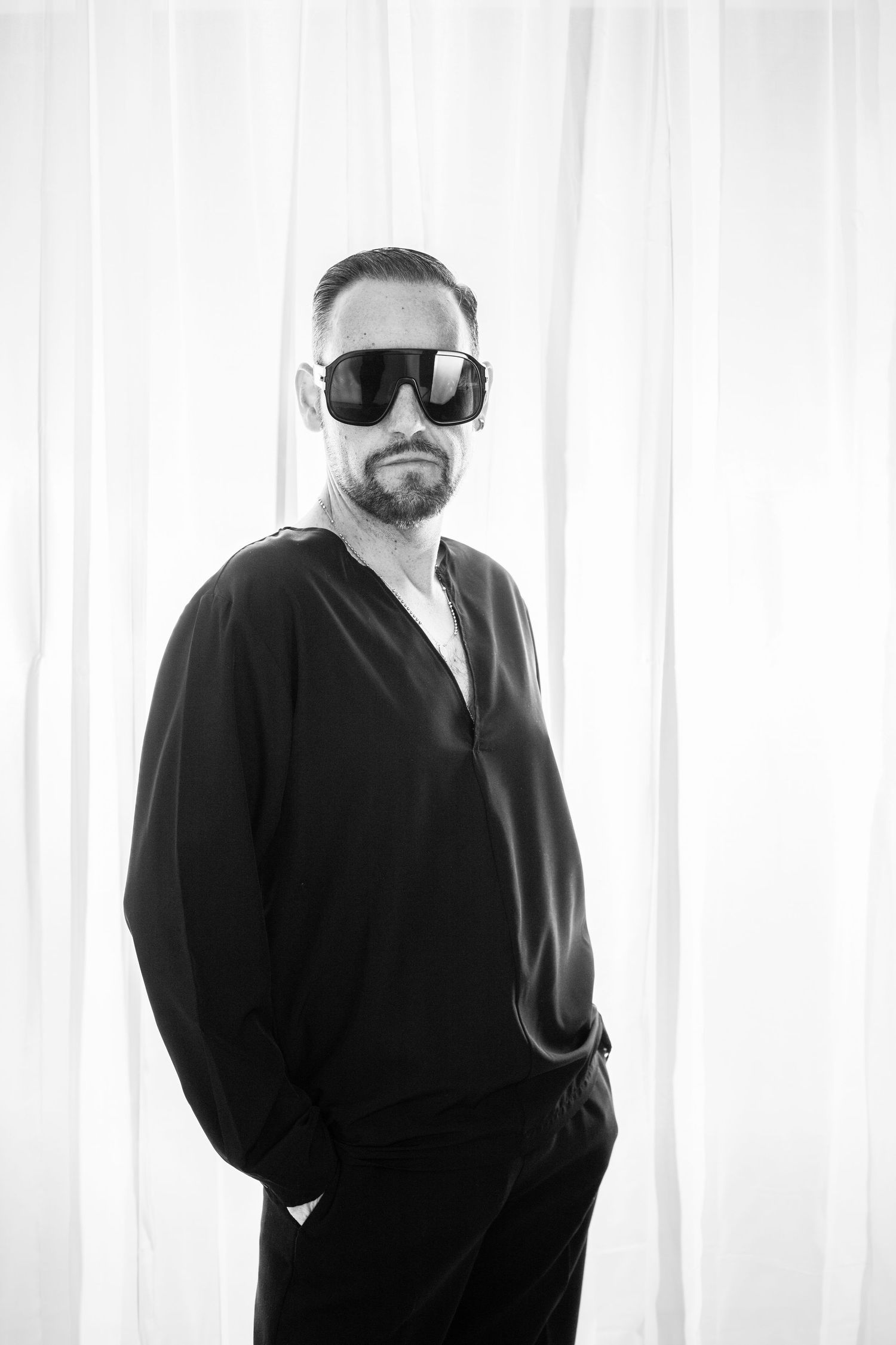 A black and white triptych of someone wearing dark clothing and sunglasses against a white curtain background.