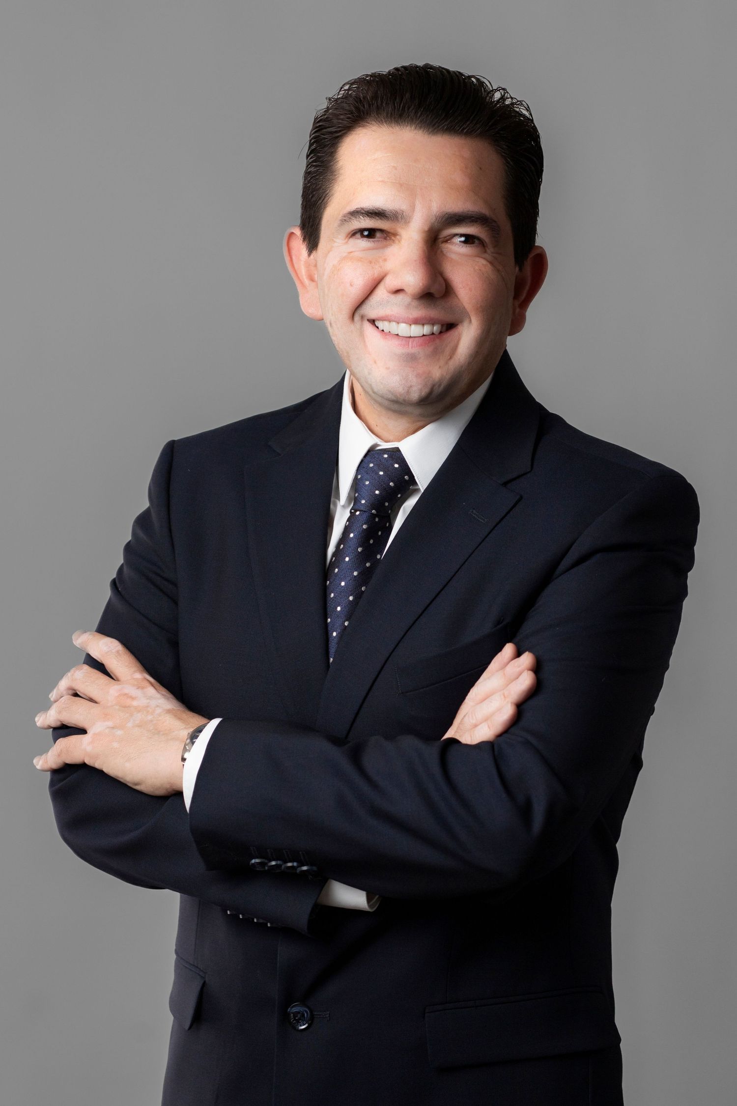 Professional portrait series showing a businessman in navy suit and polka dot tie posing with crossed arms against gray background.