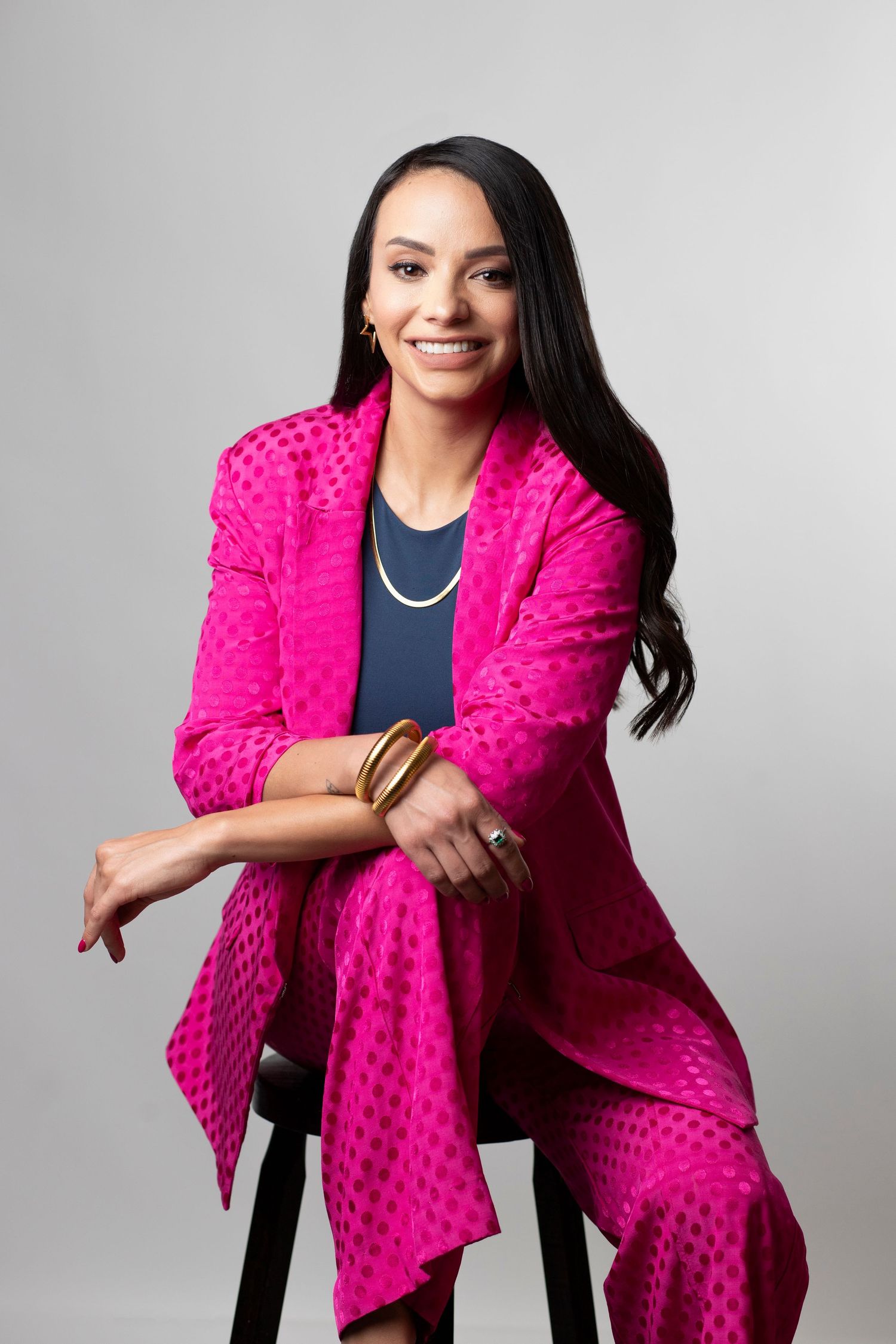 Professional portrait of someone wearing a vibrant hot pink textured blazer and matching pants against a gray background.