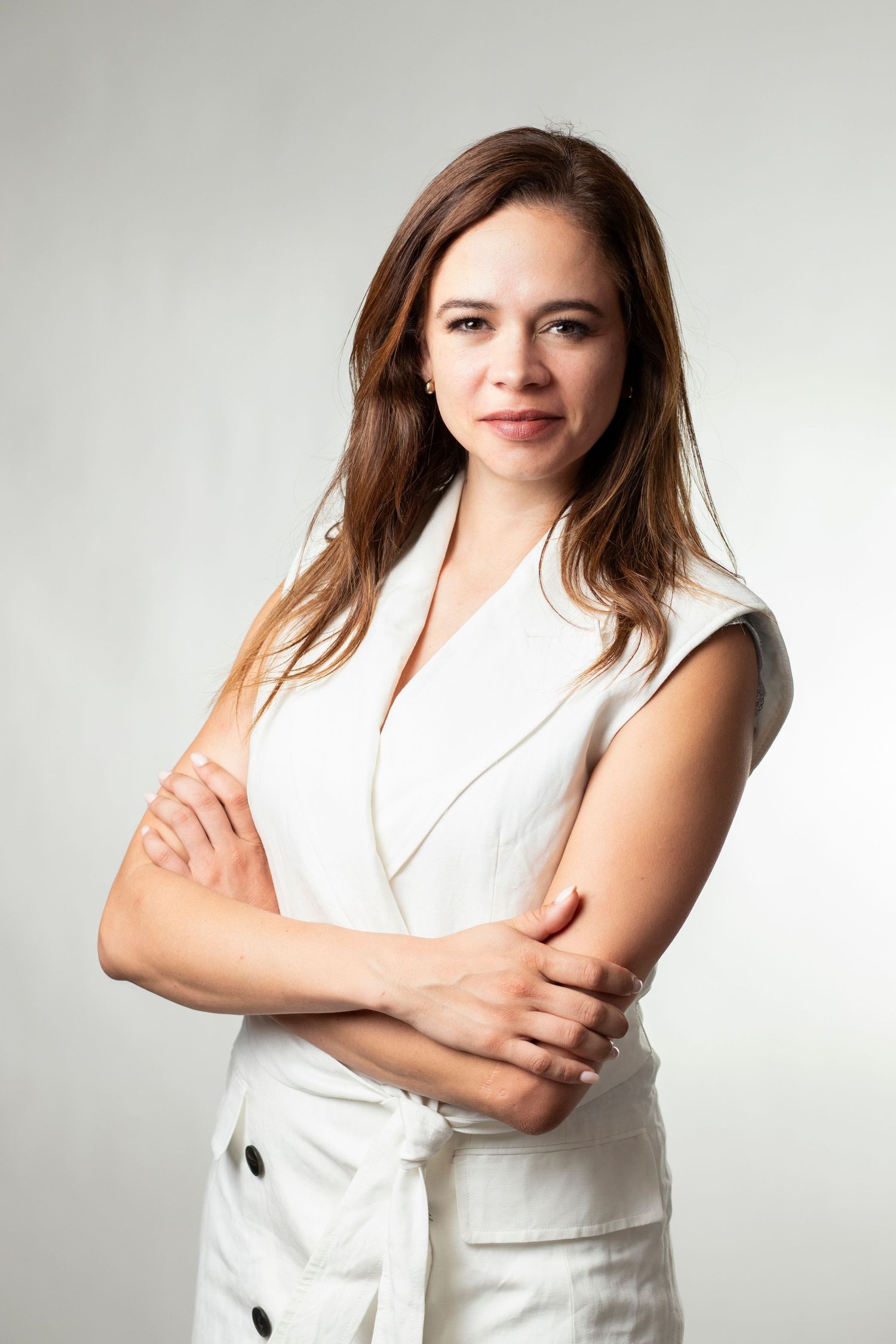 Business portrait of a person with long brown hair wearing a stylish white blazer against a light background.