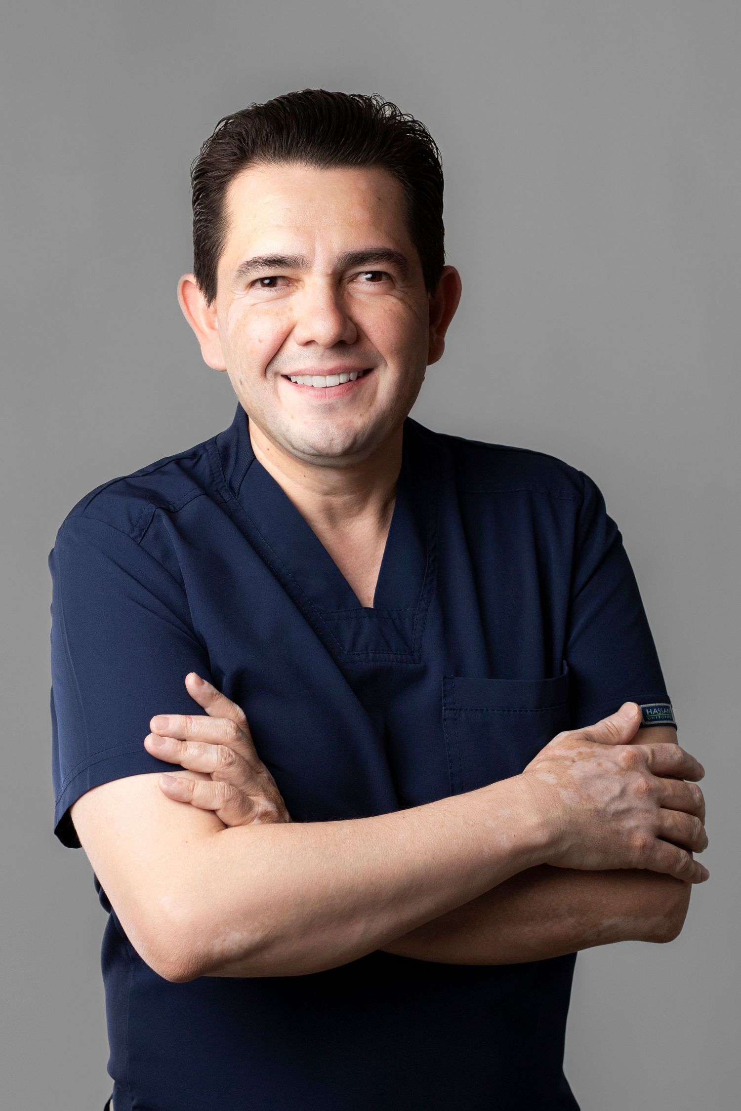Person in navy blue shirt poses with crossed arms against gray background in professional headshot series.