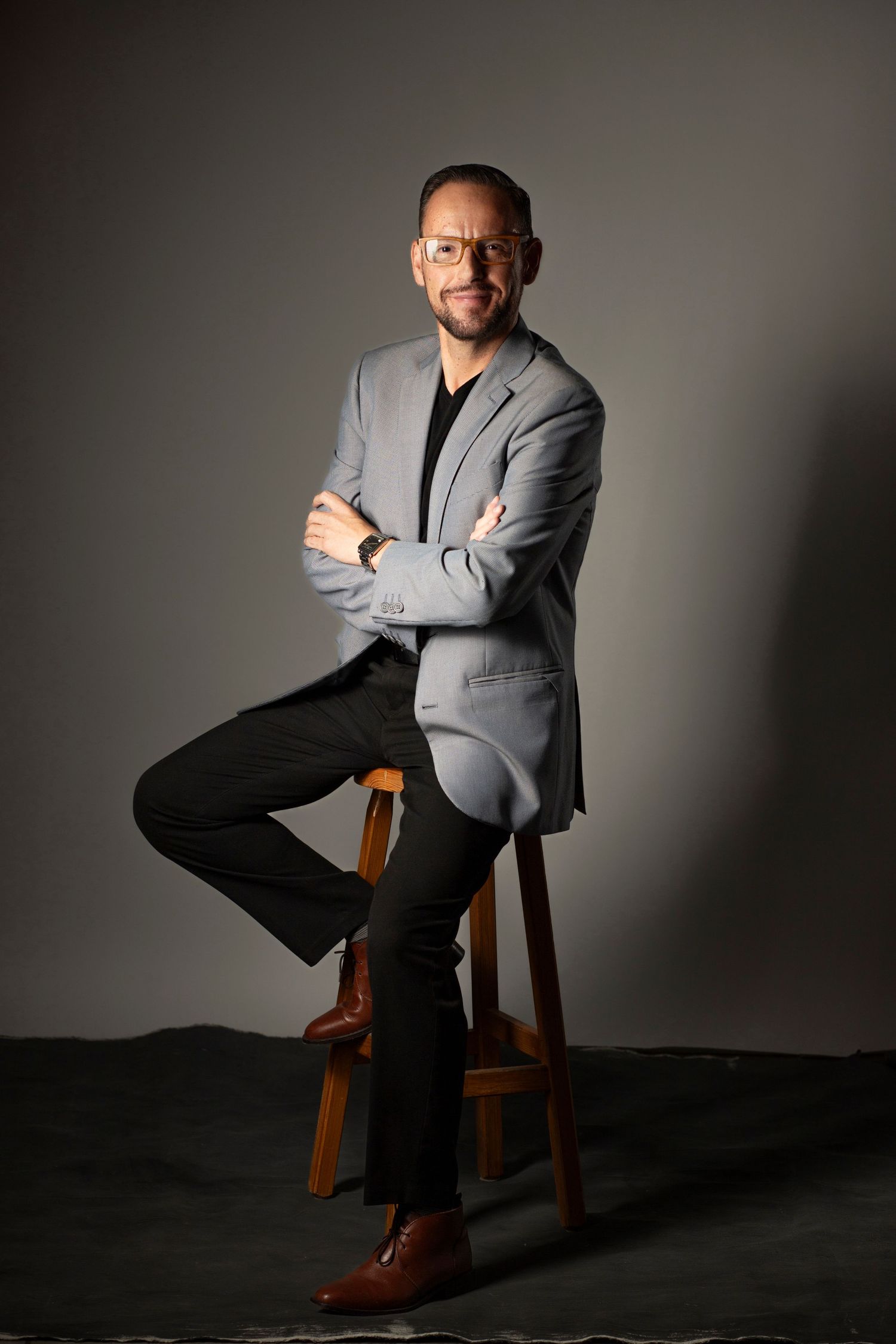 Professional studio portrait series showing a person in a gray suit seated on a wooden chair against dark backdrop.