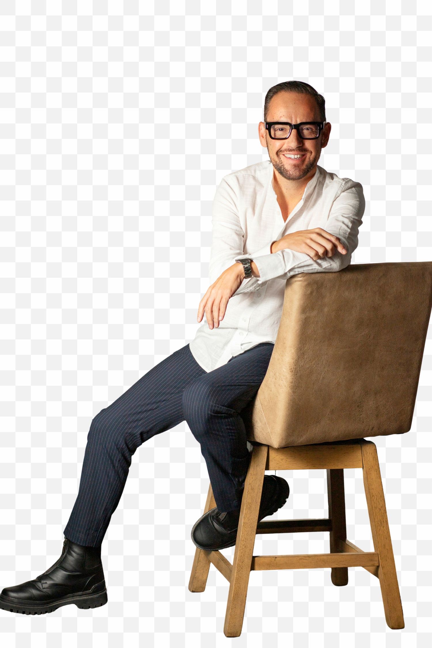 A person in glasses and a white shirt sits casually on a wooden chair against a transparent background.
