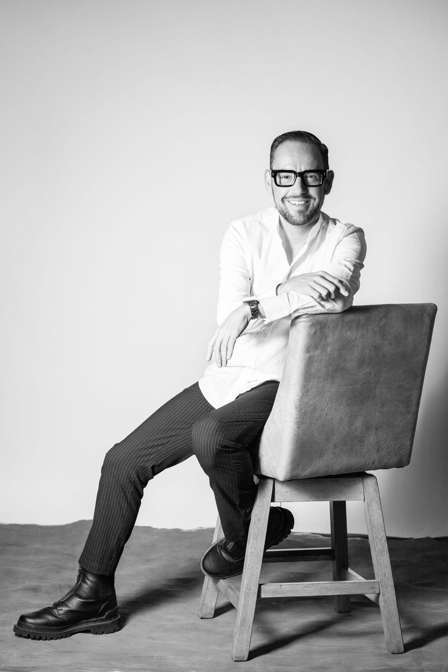 Minimalist black and white photographs of someone seated in casual attire on a simple chair.